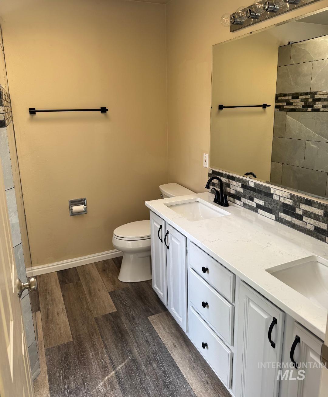 Bathroom with double vanity, dark wood finished floors, a shower, and decorative backsplash