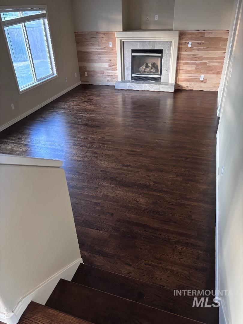 Unfurnished living room with a fireplace, wooden walls, and dark wood-style floors