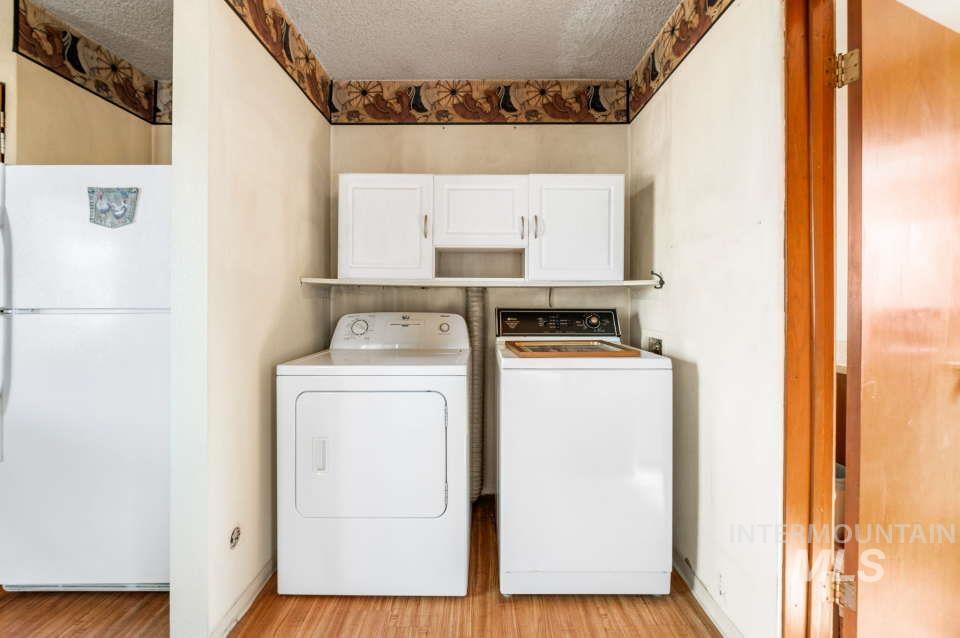 Washroom featuring independent washer and dryer, cabinet space, light wood-type flooring, and a textured ceiling