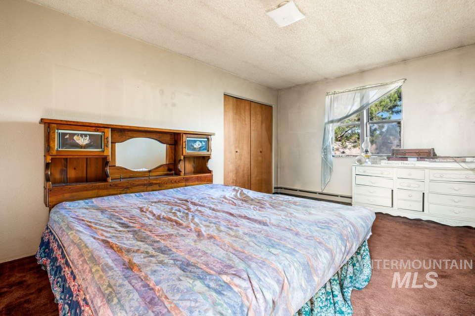 Bedroom featuring a baseboard heating unit, carpet, a textured ceiling, and a closet