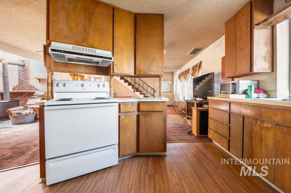 Kitchen with extractor fan, electric stove, a textured ceiling, wood finished floors, and brown cabinets