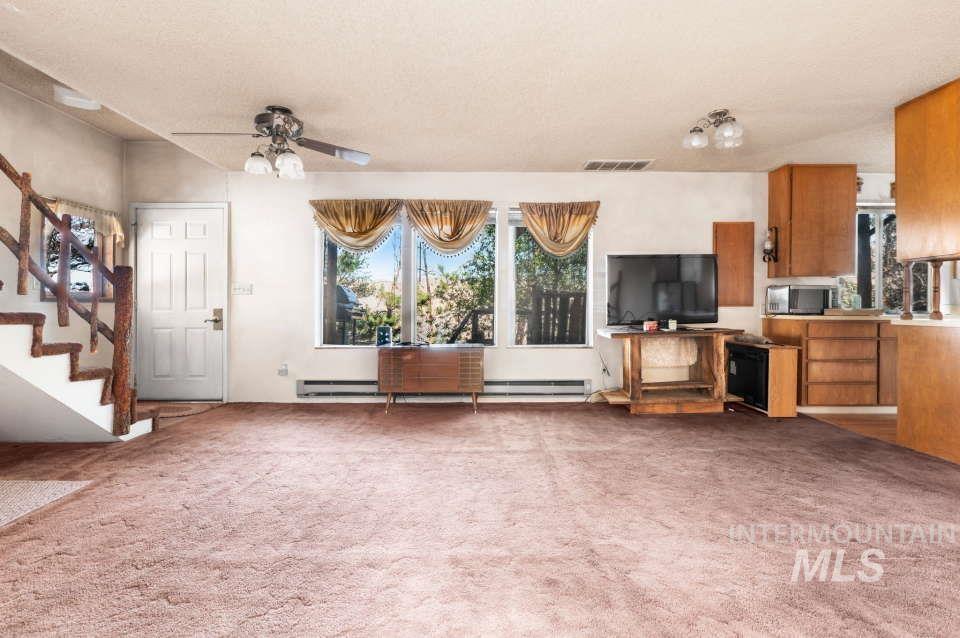 Unfurnished living room with stairs, carpet flooring, and a ceiling fan