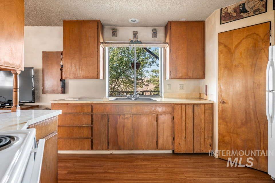 Kitchen featuring white appliances, light countertops, wood finished floors, a textured ceiling, and brown cabinetry