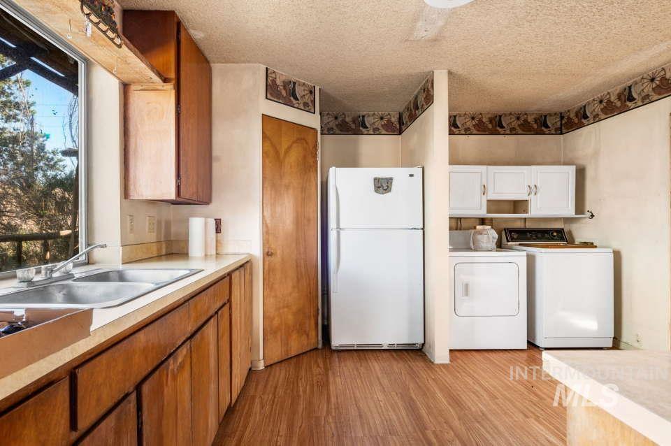 Kitchen featuring freestanding refrigerator, washer and clothes dryer, light countertops, light wood-style floors, and a textured ceiling