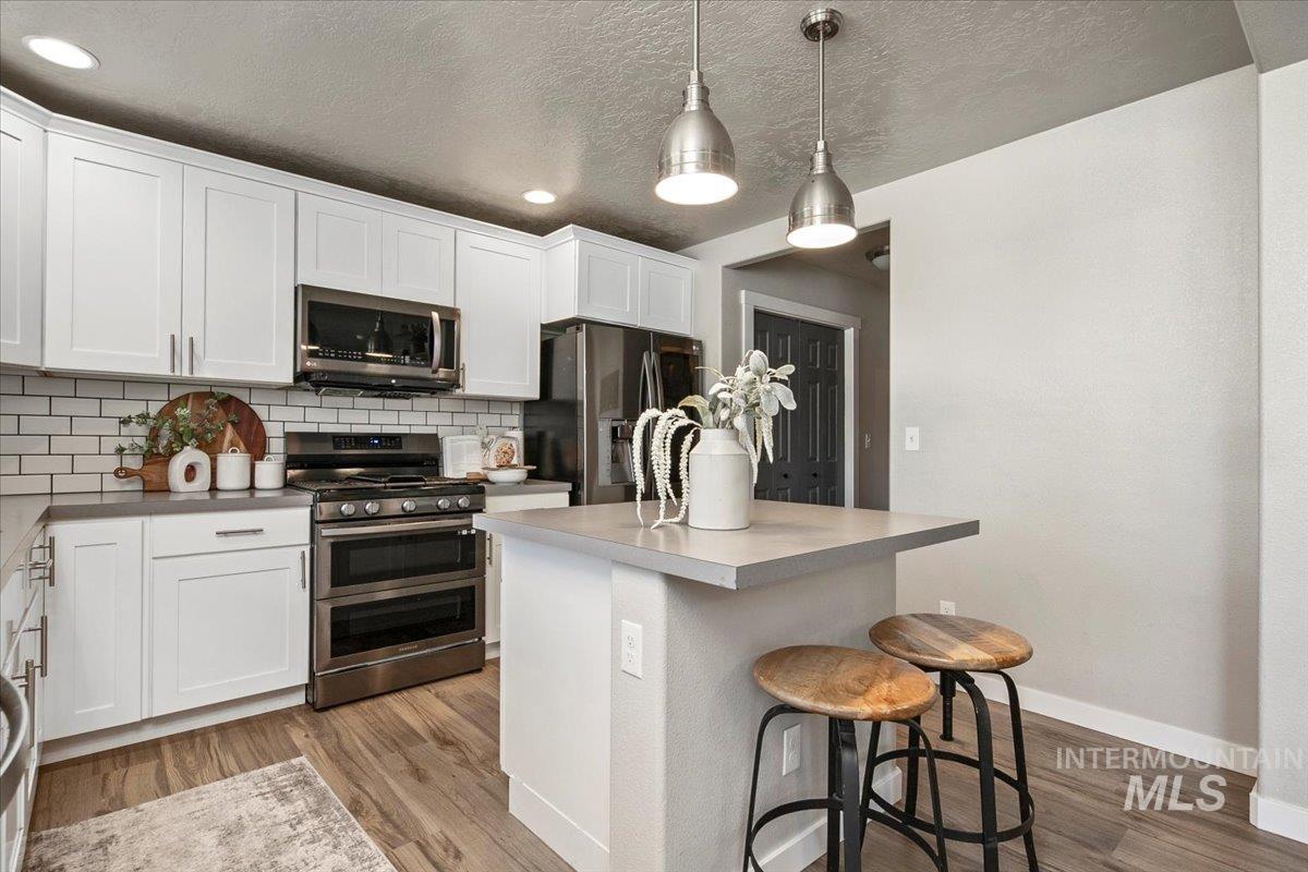 Kitchen with appliances with stainless steel finishes, decorative backsplash, a breakfast bar area, white cabinets, and a textured ceiling