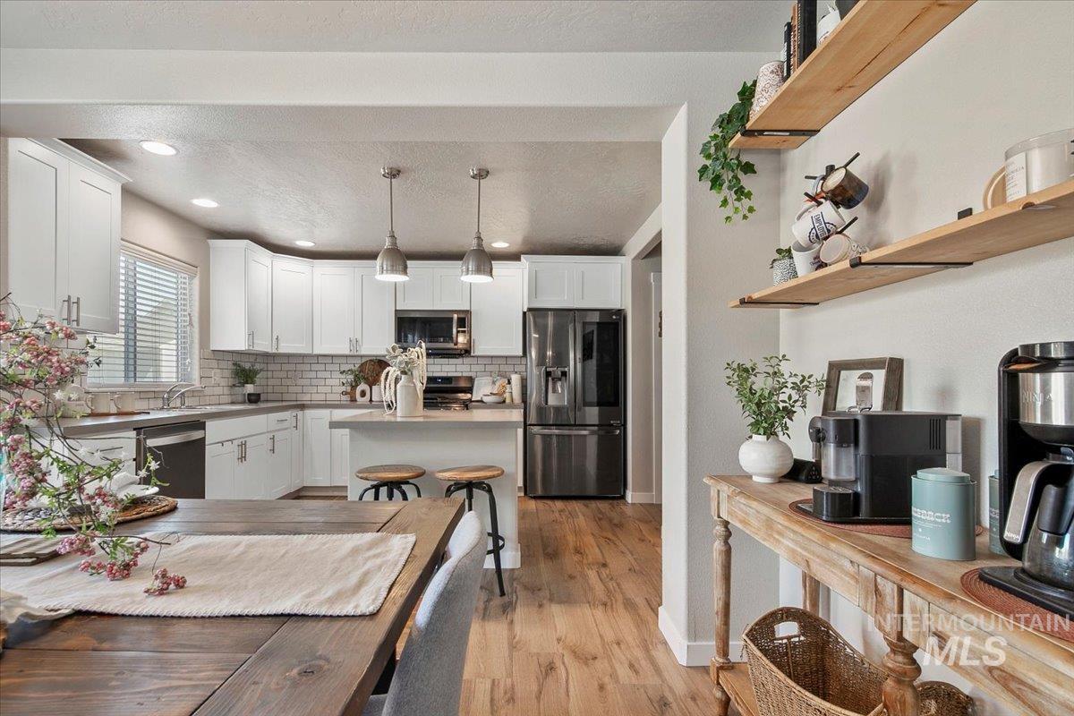 Kitchen with a kitchen island, pendant lighting, appliances with stainless steel finishes, white cabinets, and tasteful backsplash