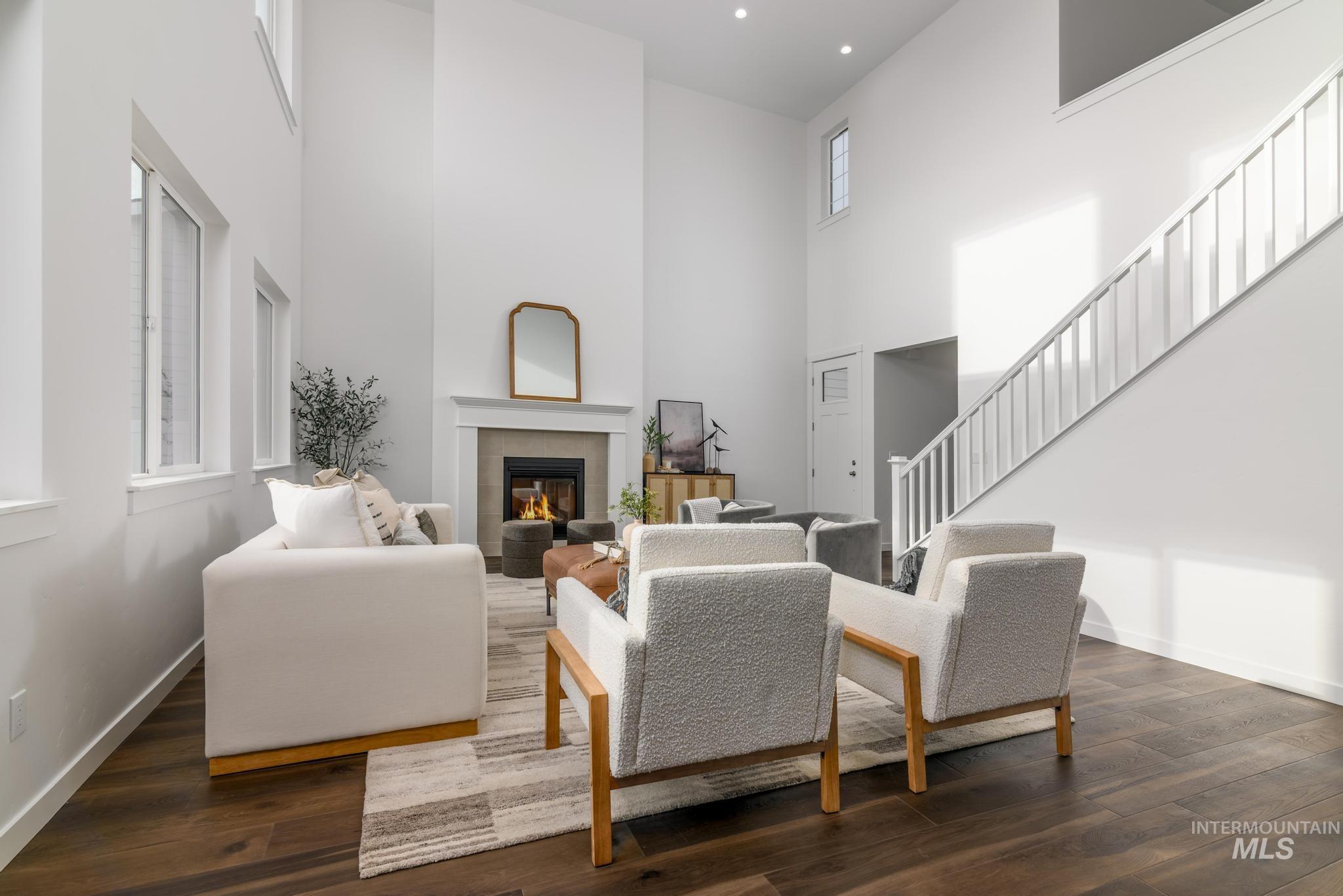 Living room featuring a tiled fireplace, dark wood-style floors, a towering ceiling, and stairway