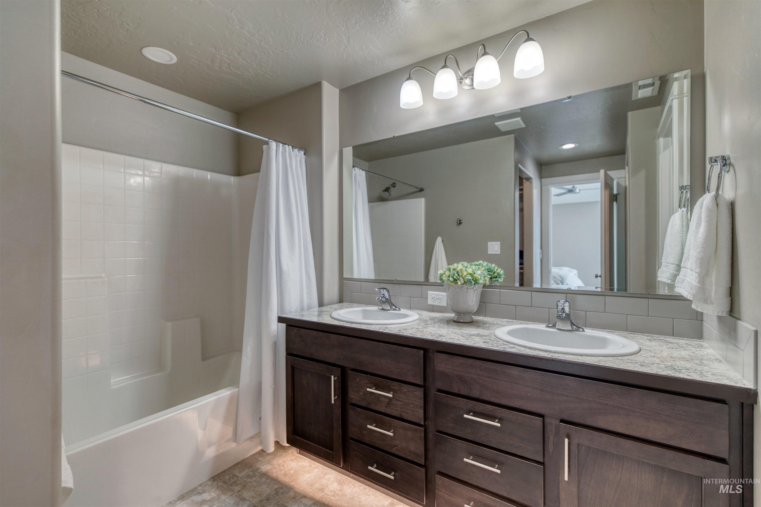 Bathroom featuring double vanity, shower / tub combo, decorative backsplash, recessed lighting, and a textured ceiling