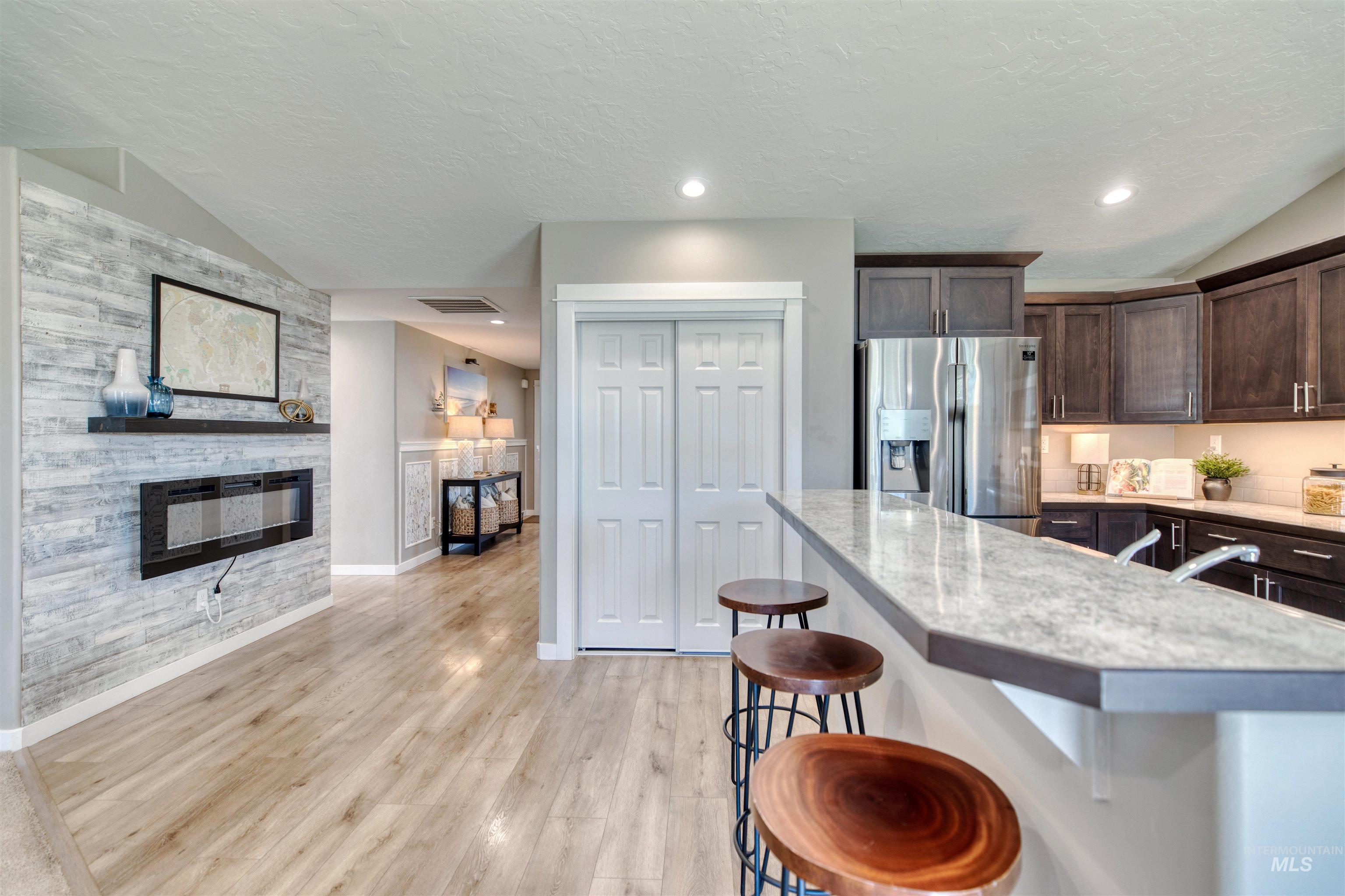 Kitchen featuring dark wood finish cabinets, a kitchen bar, stainless steel fridge, light wood-style floors, and a stone fireplace
