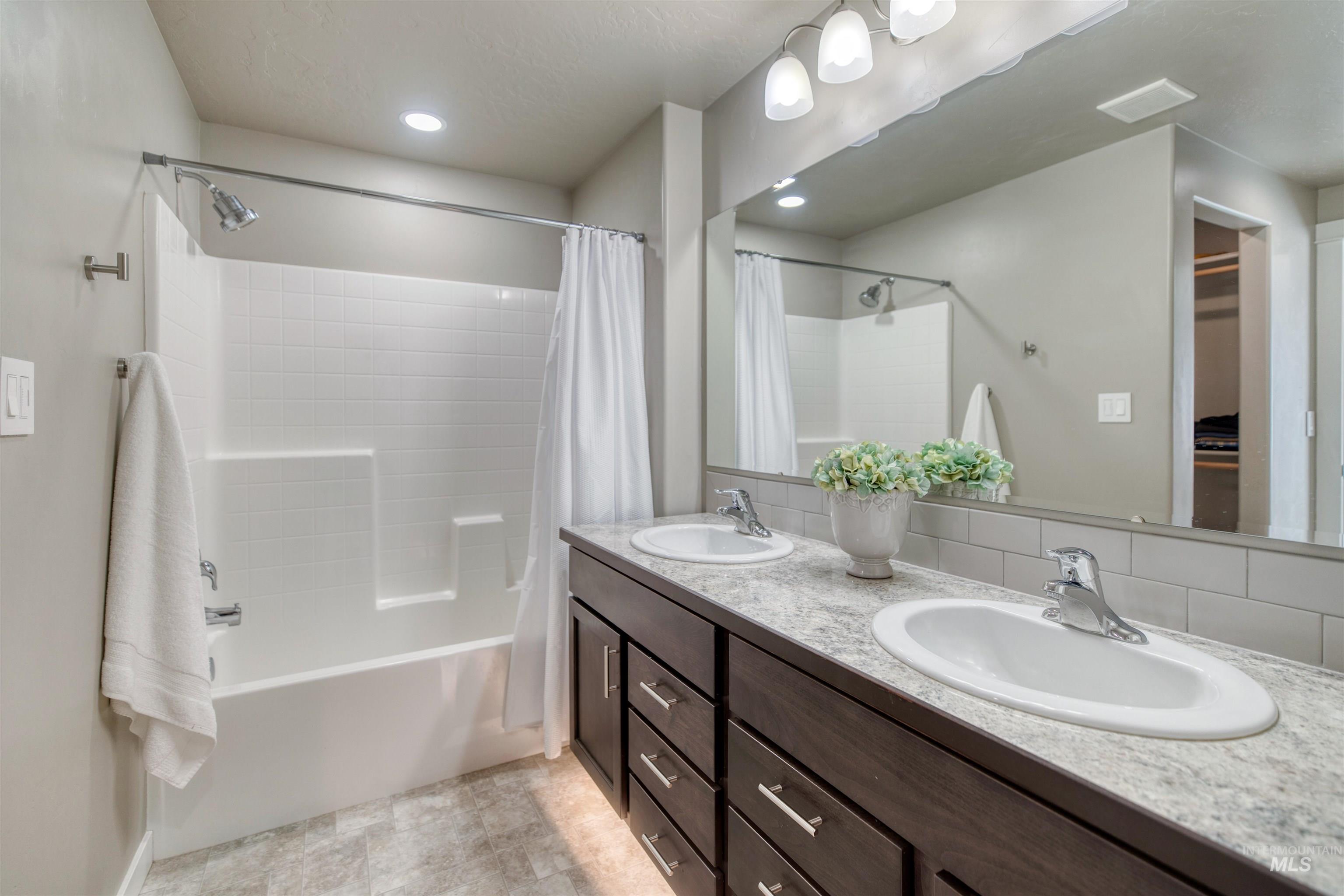 Full bathroom with double vanity, shower / bath combo with shower curtain, and a spacious closet