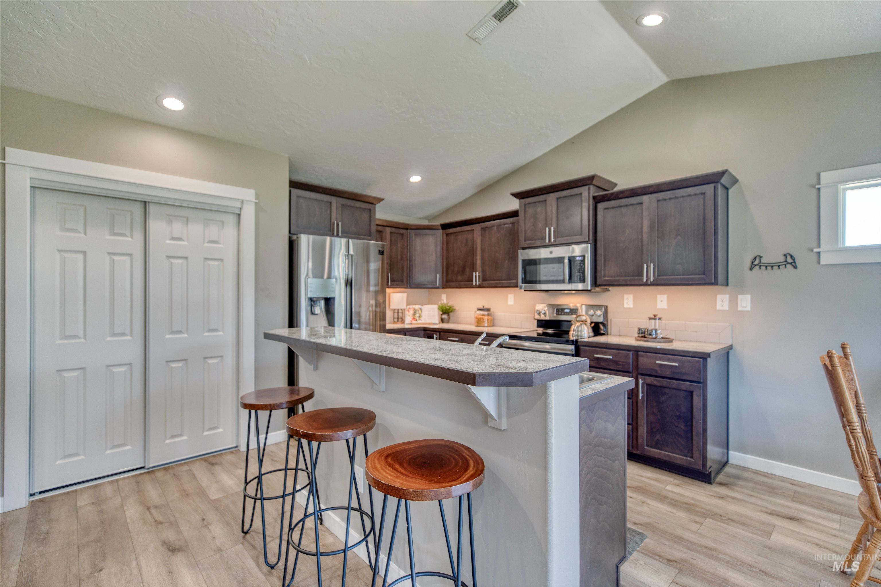 Kitchen featuring a breakfast bar, dark wood finish cabinets, stainless steel appliances, light wood-style floors, and light countertops