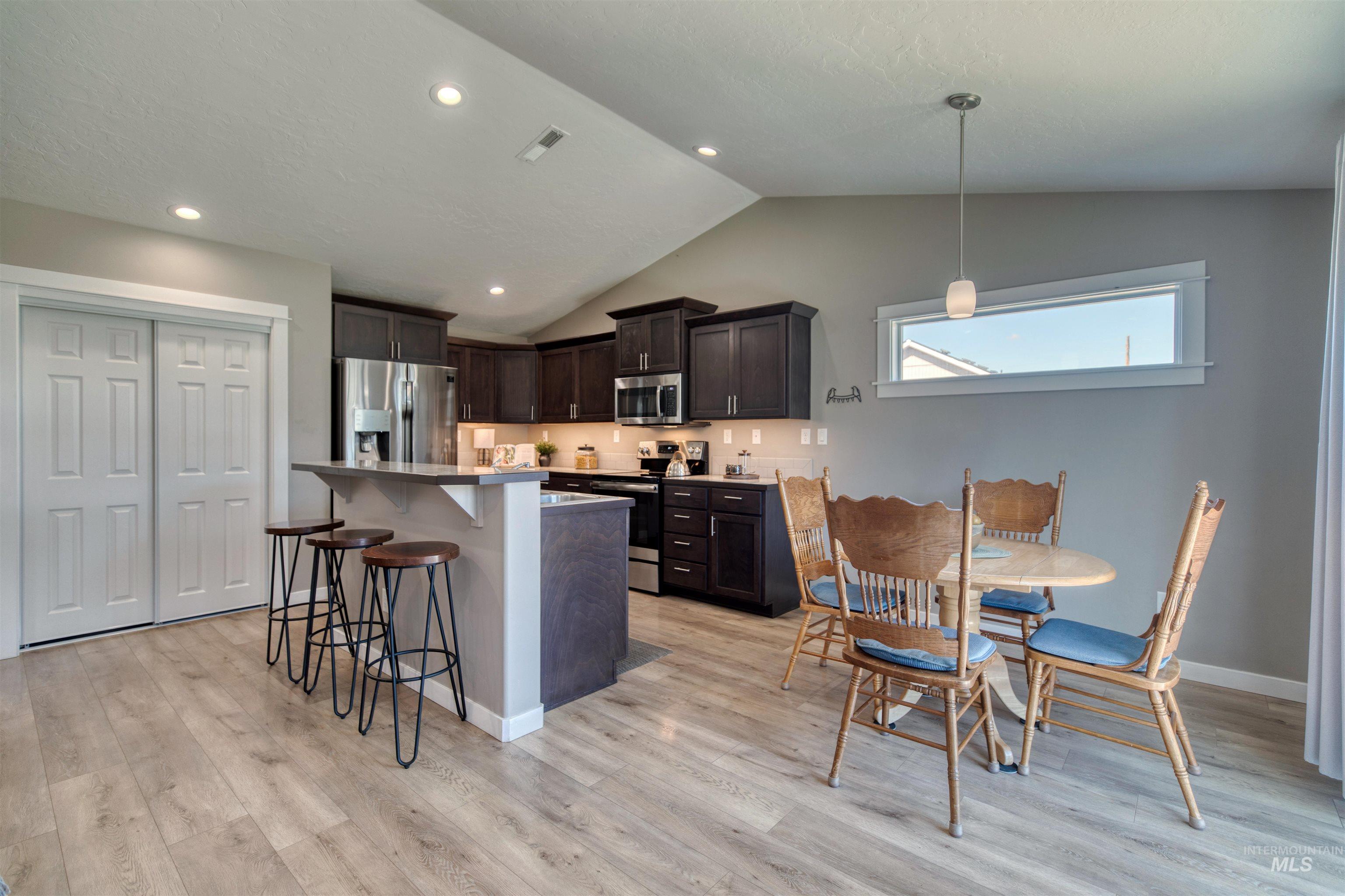 Kitchen featuring dark wood finish cabinets, a kitchen bar, stainless steel appliances, light countertops, and pendant lighting