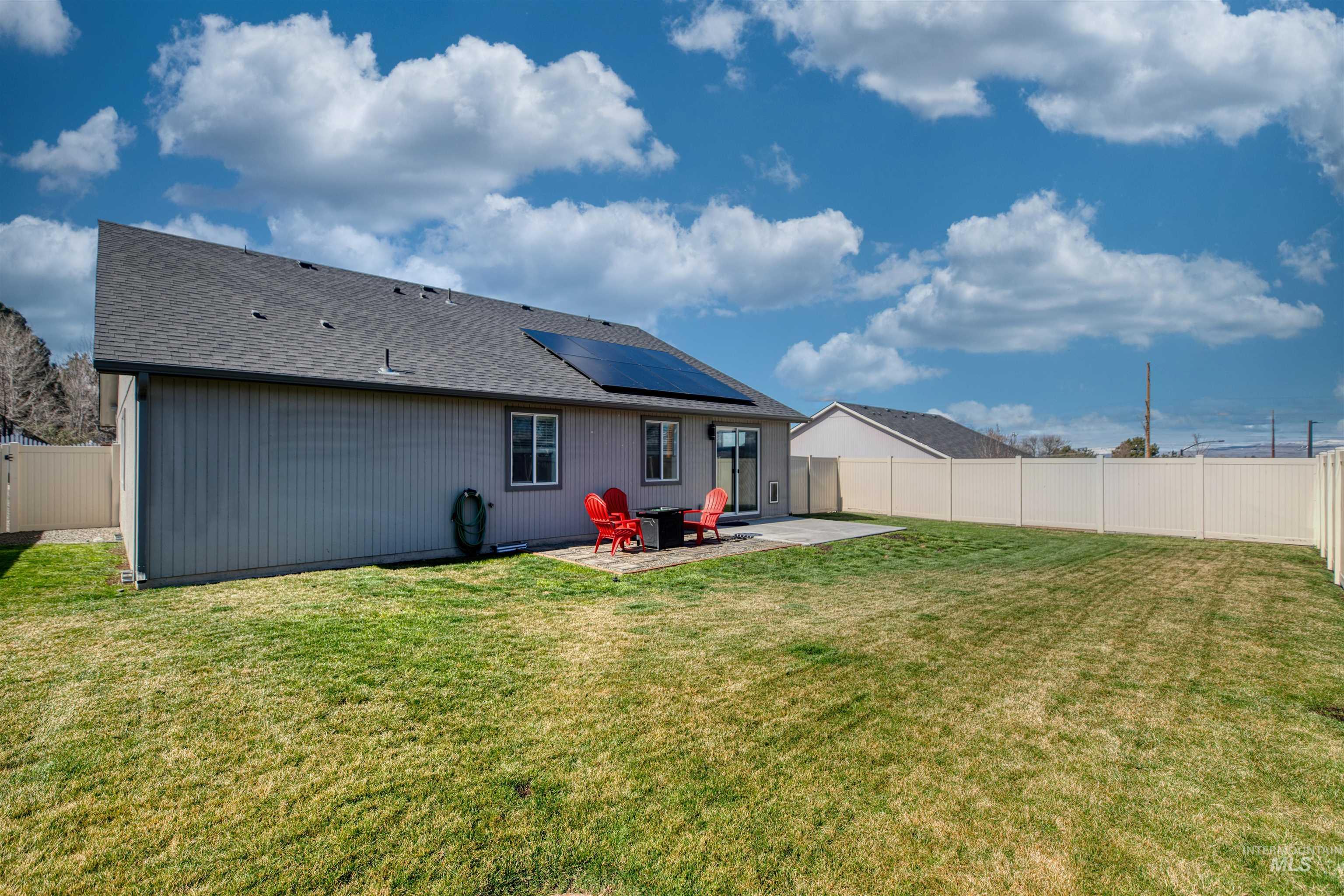 Back of property with roof mounted solar panels, a patio, a fenced backyard, and roof with shingles