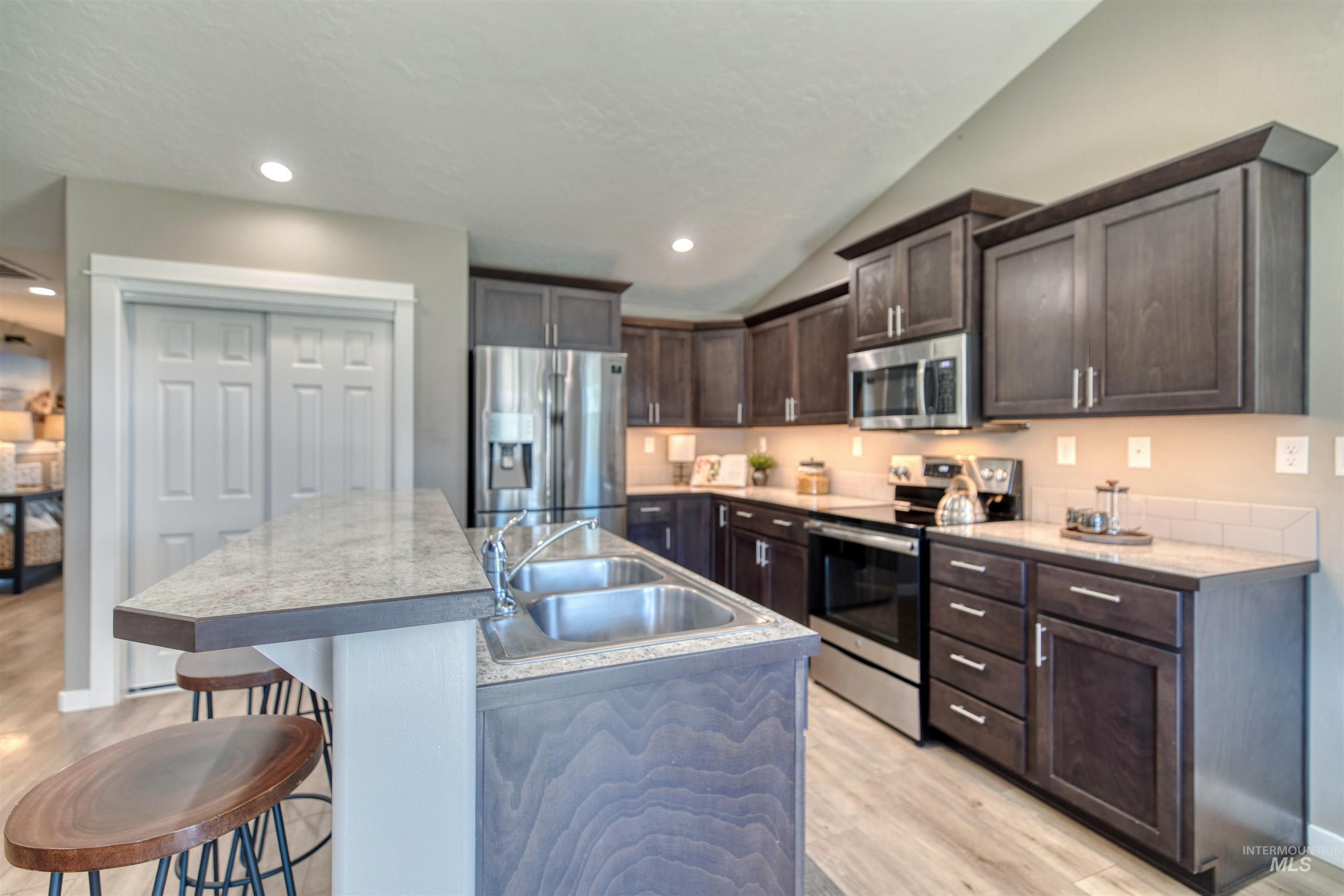Kitchen with stainless steel appliances, dark wood finish cabinetry, light wood finished floors, a kitchen bar, and lofted ceiling