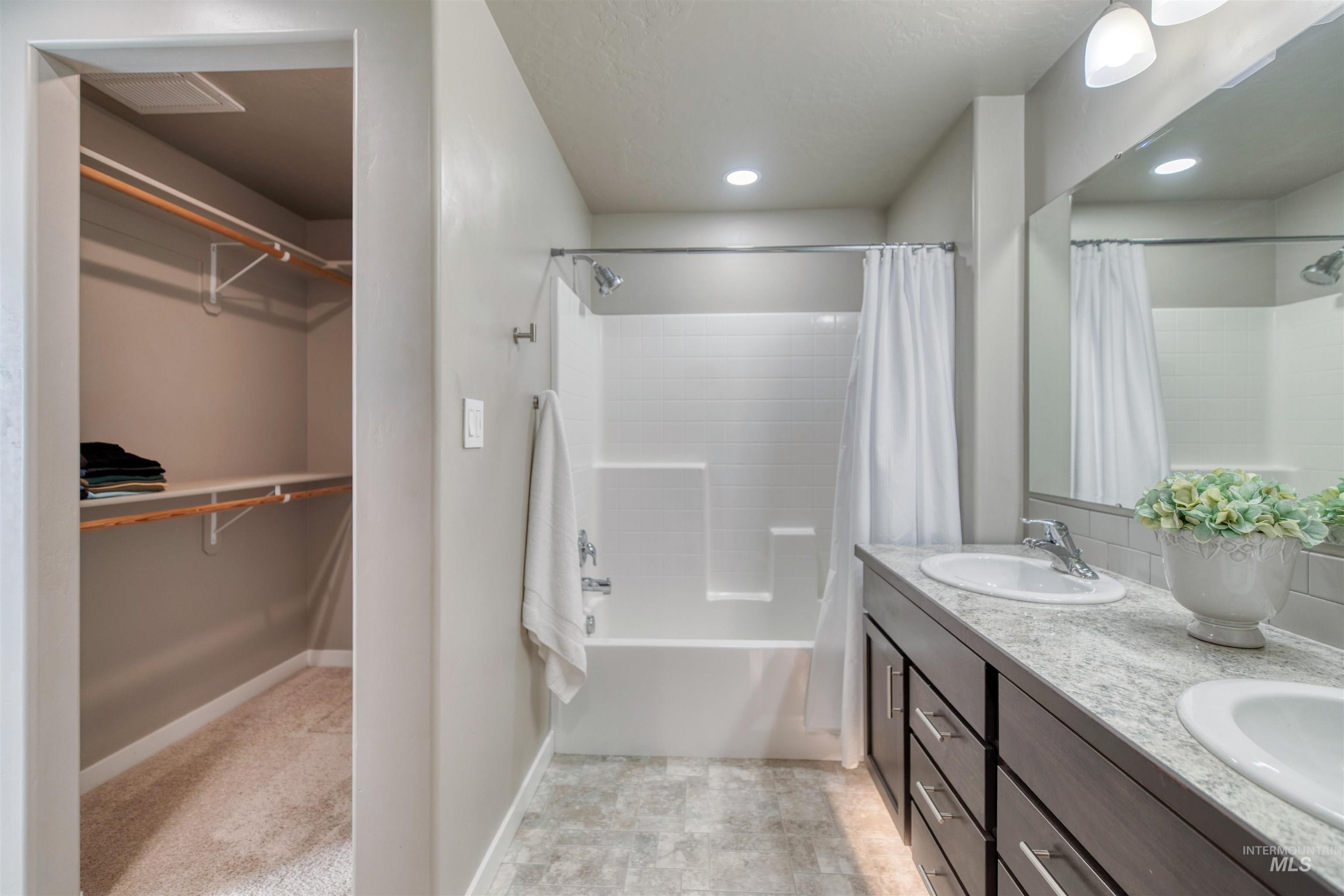 Bathroom with double vanity, a spacious closet, and shower / bath combo with shower curtain