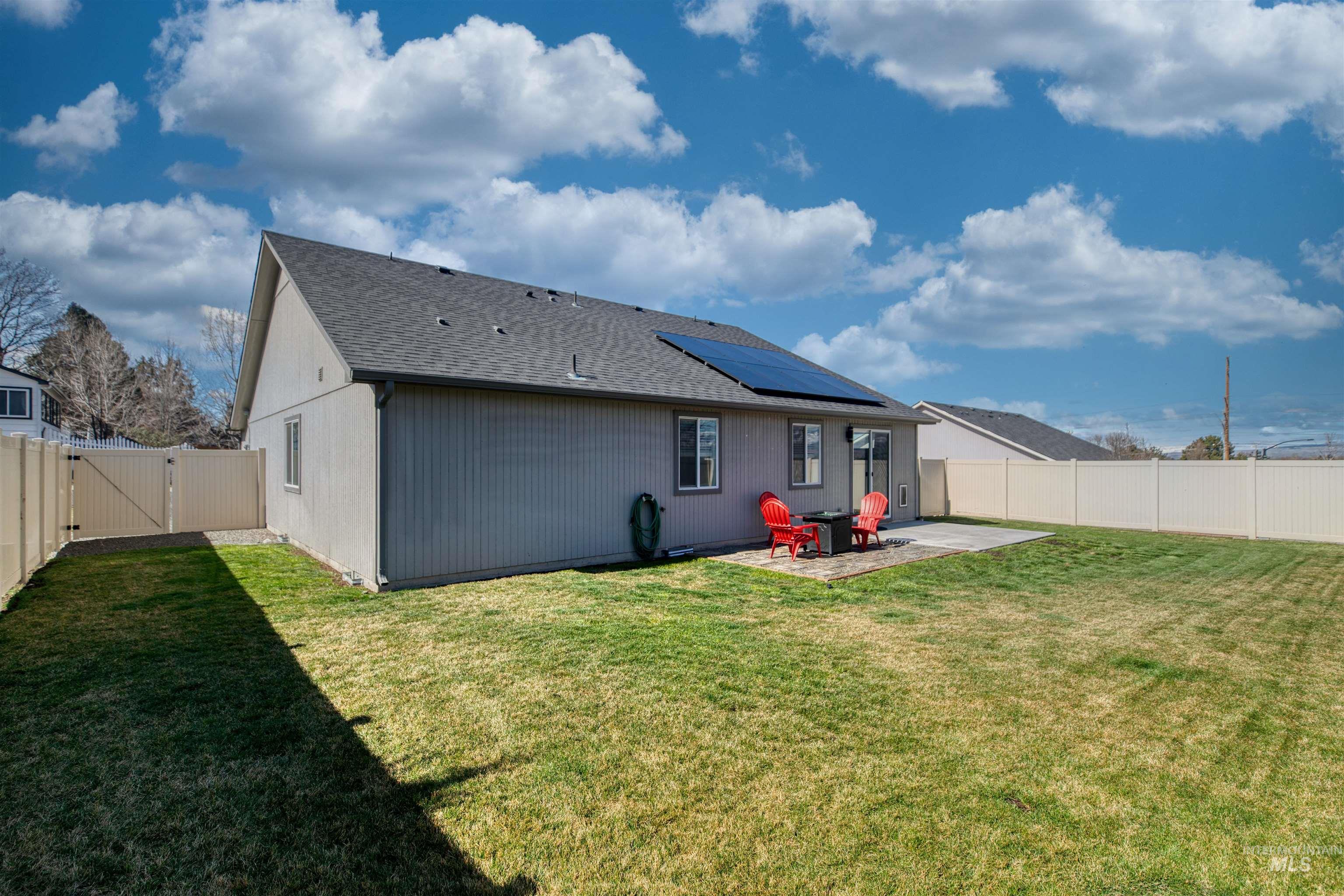 Rear view of property with a gate, a fenced backyard, a patio, roof mounted solar panels, and a shingled roof