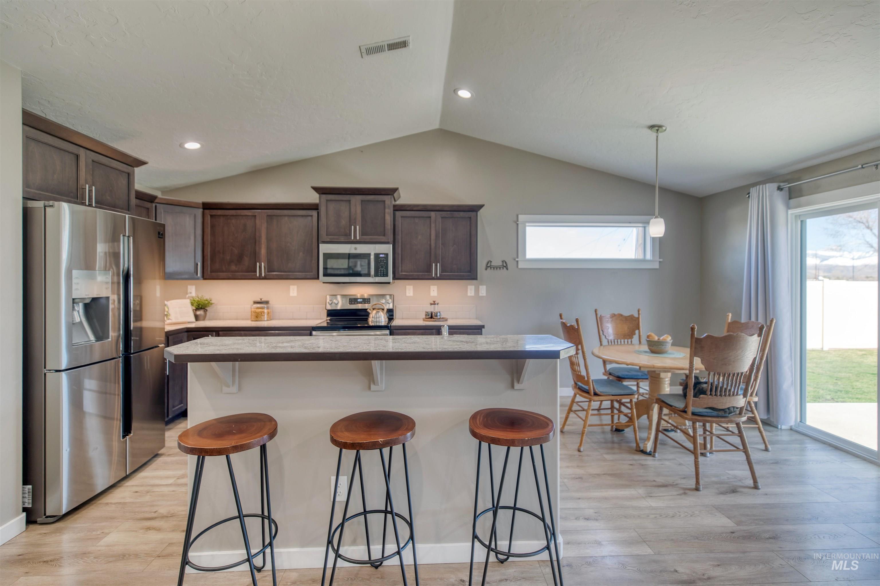 Kitchen with stainless steel appliances, a breakfast bar area, dark wood finish cabinets, light wood-style flooring, and decorative light fixtures