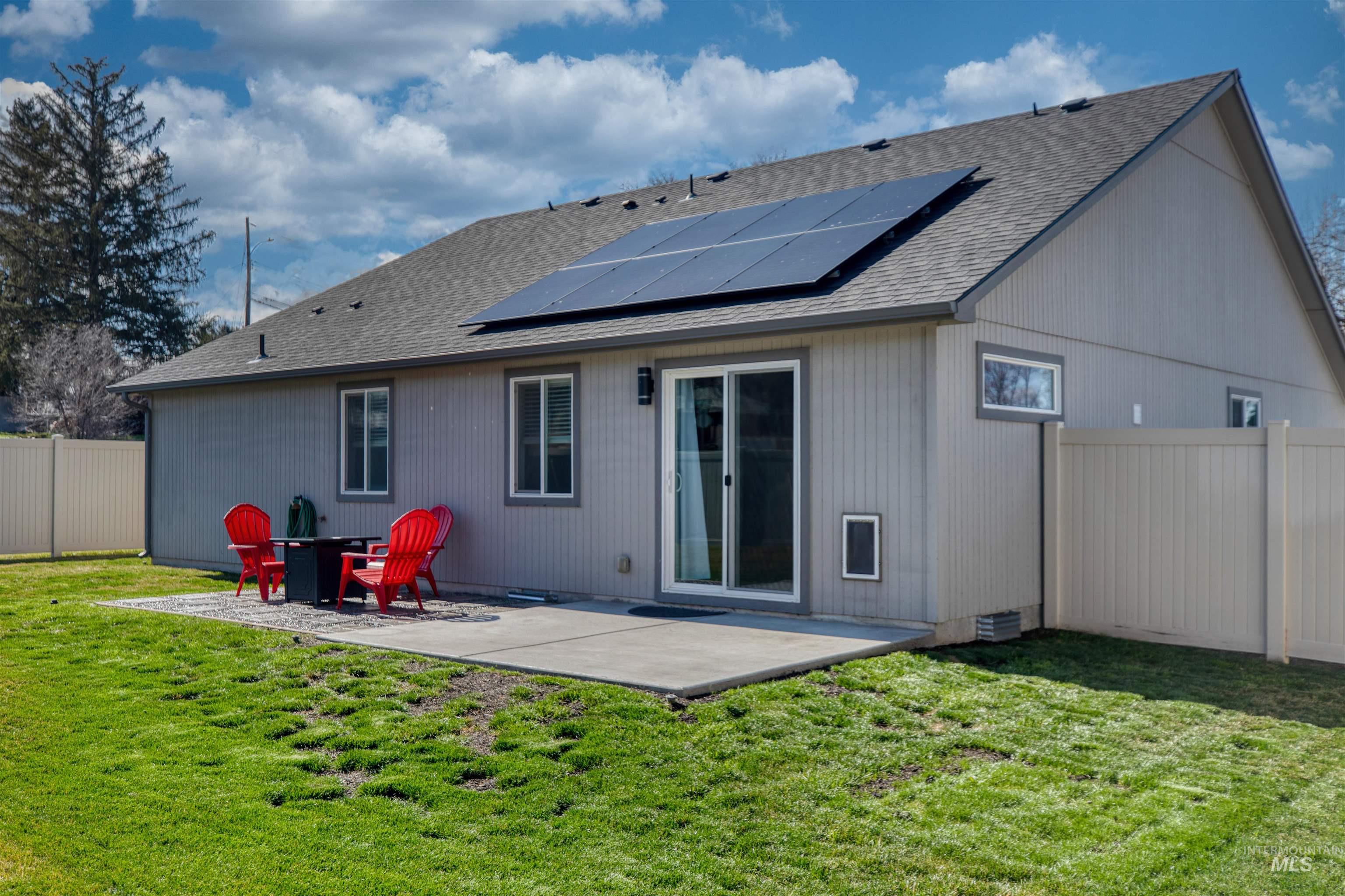 Back of house with a fenced backyard, roof with shingles, a patio area, and solar panels