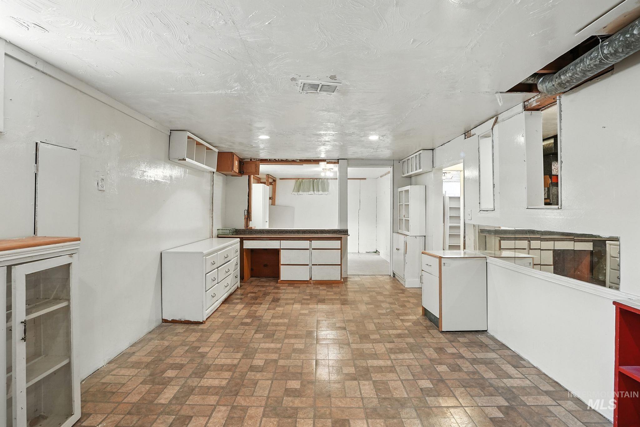 Kitchen with brick patterned flooring, open shelves, brown cabinetry, a textured ceiling, and white cabinets