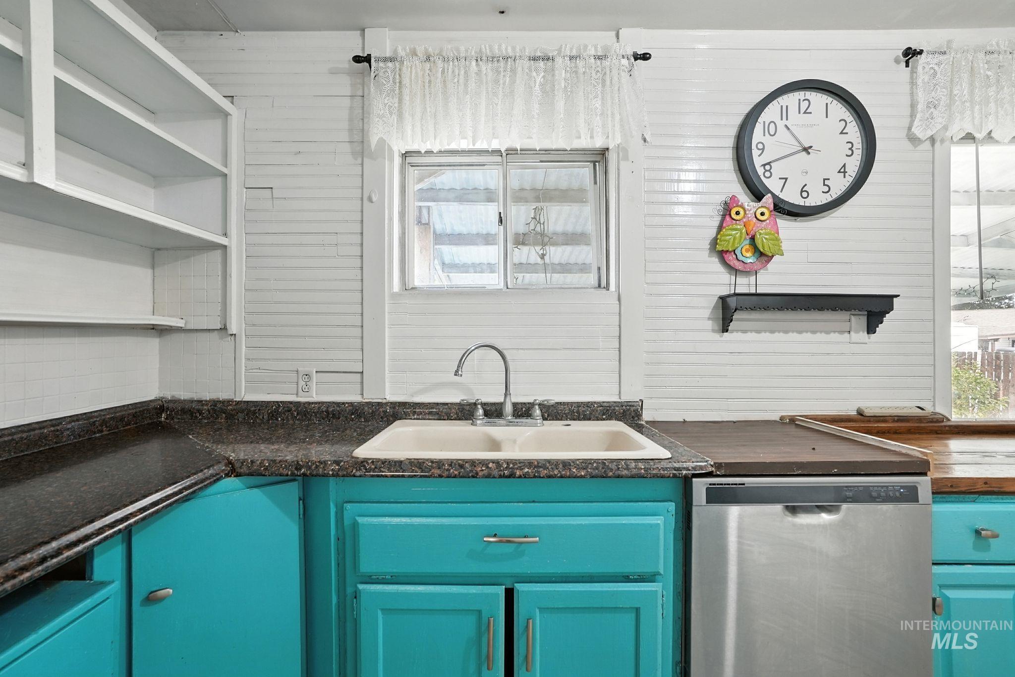 Kitchen with dishwasher, dark countertops, blue cabinetry, and open shelves
