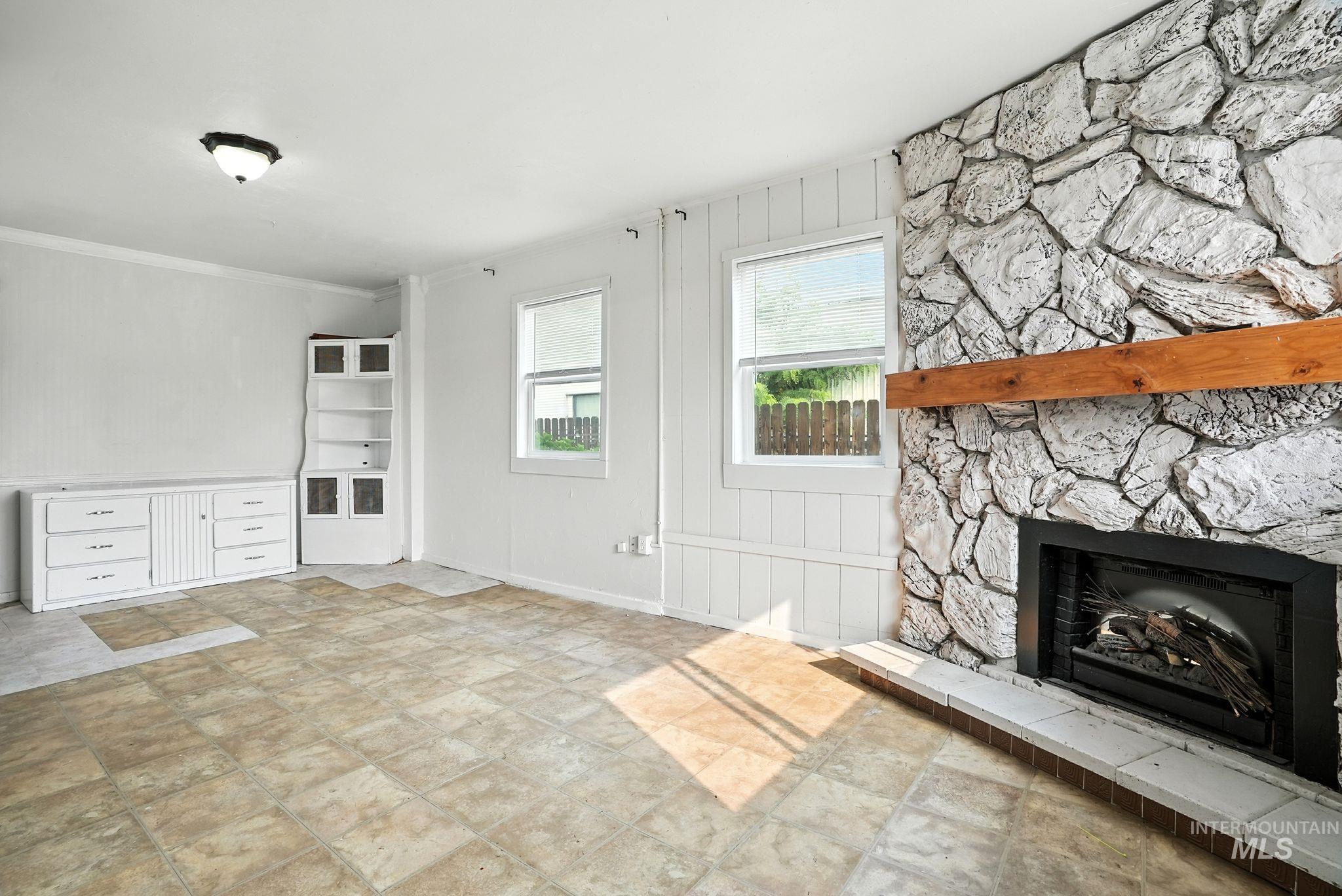 Unfurnished living room with a stone fireplace and crown molding