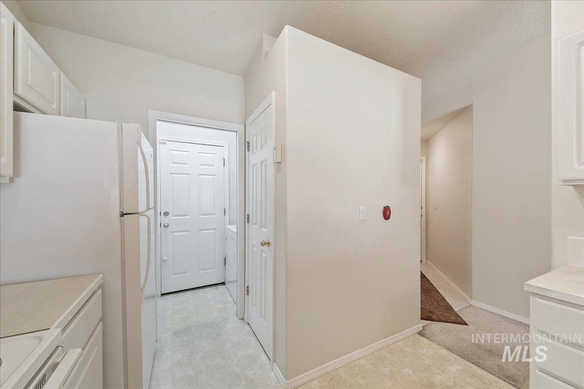 Kitchen featuring freestanding refrigerator, white cabinetry, light countertops, range, and a textured ceiling