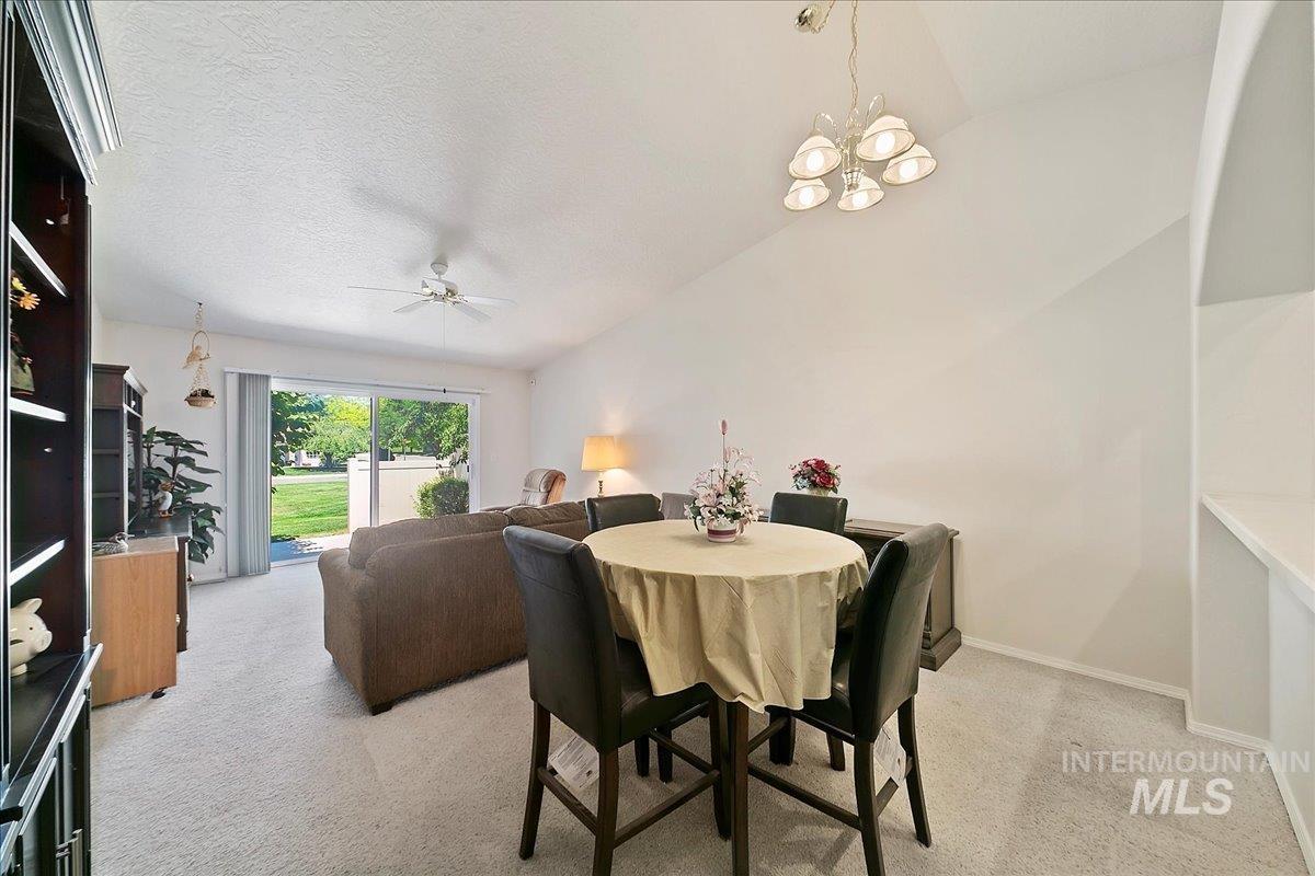 Dining room featuring light colored carpet, vaulted ceiling, a ceiling fan, a textured ceiling, and a chandelier