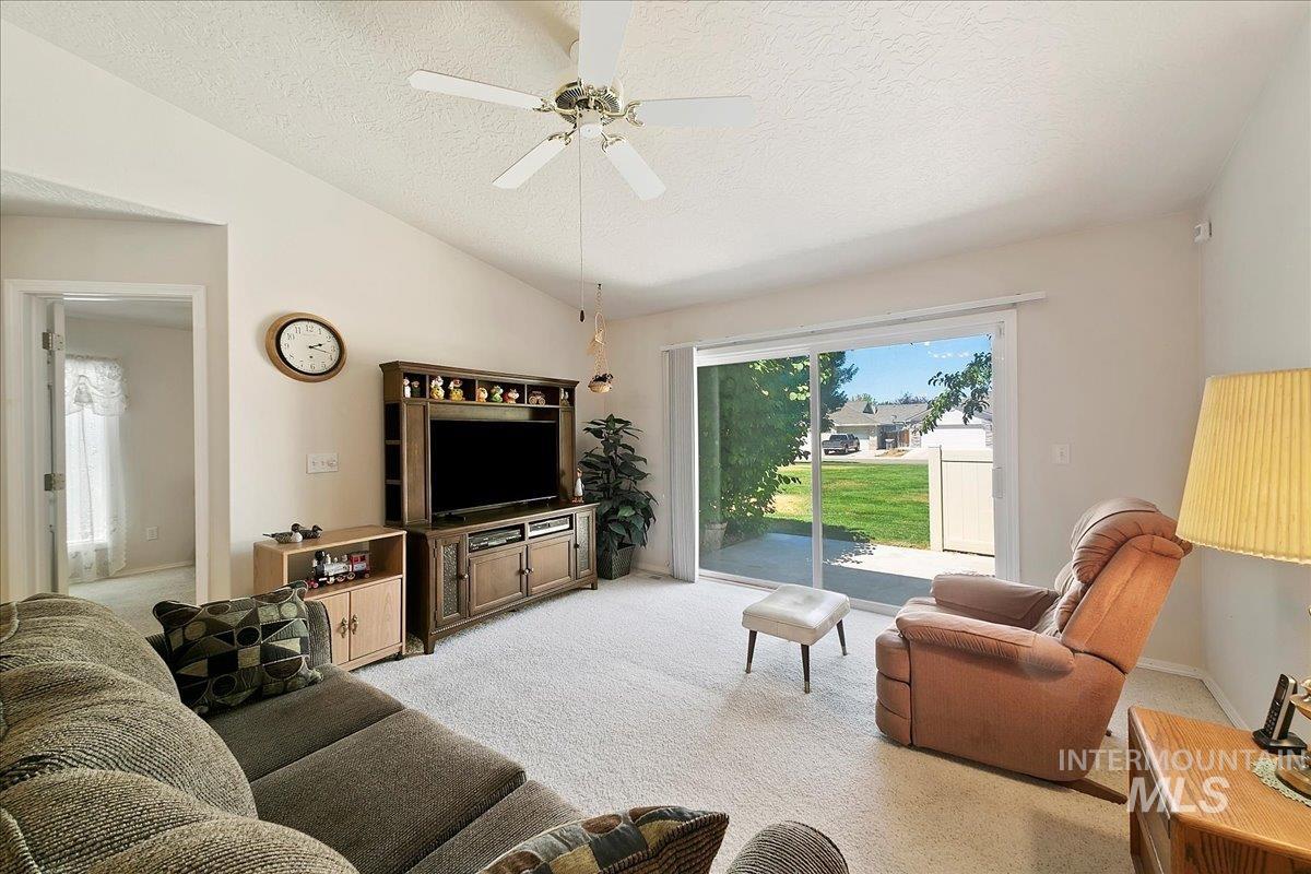 Living area with lofted ceiling, a textured ceiling, light carpet, and ceiling fan