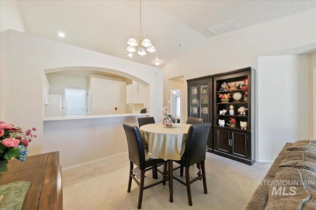Dining room featuring a chandelier, light colored carpet, lofted ceiling, and arched walkways