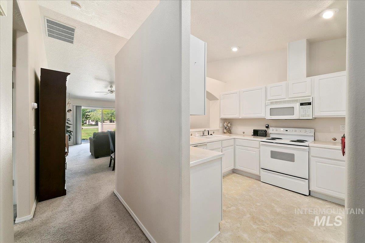 Kitchen with white appliances, white cabinetry, a textured ceiling, light countertops, and ceiling fan