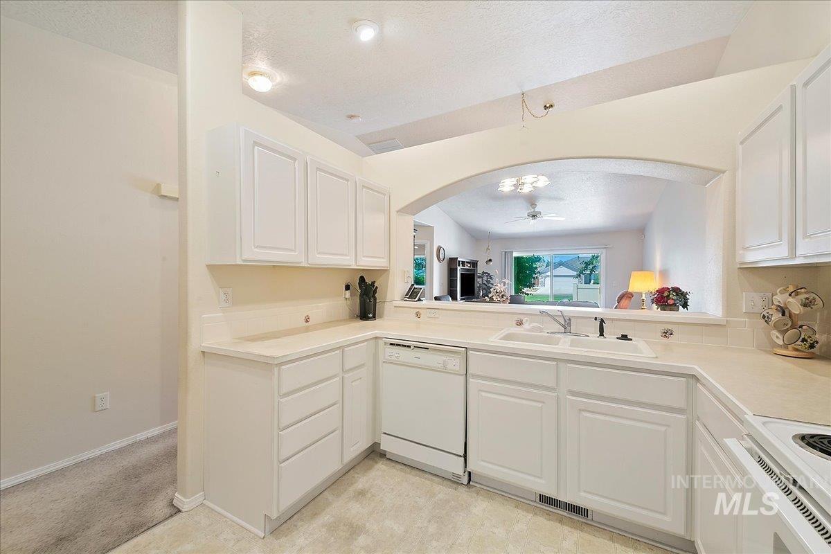 Kitchen with arched walkways, a textured ceiling, white appliances, white cabinetry, and a ceiling fan