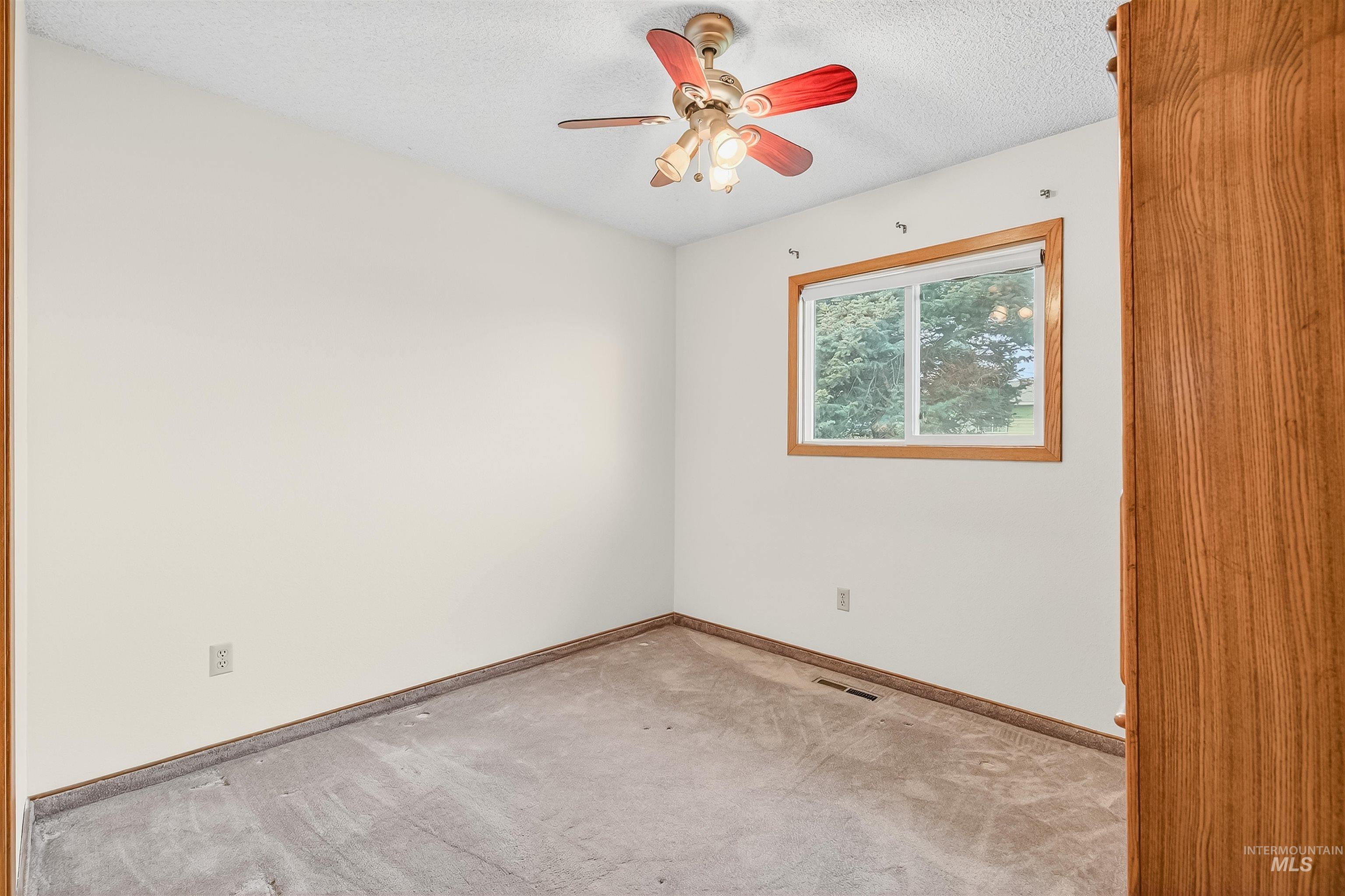 Empty room featuring light carpet, a textured ceiling, and a ceiling fan