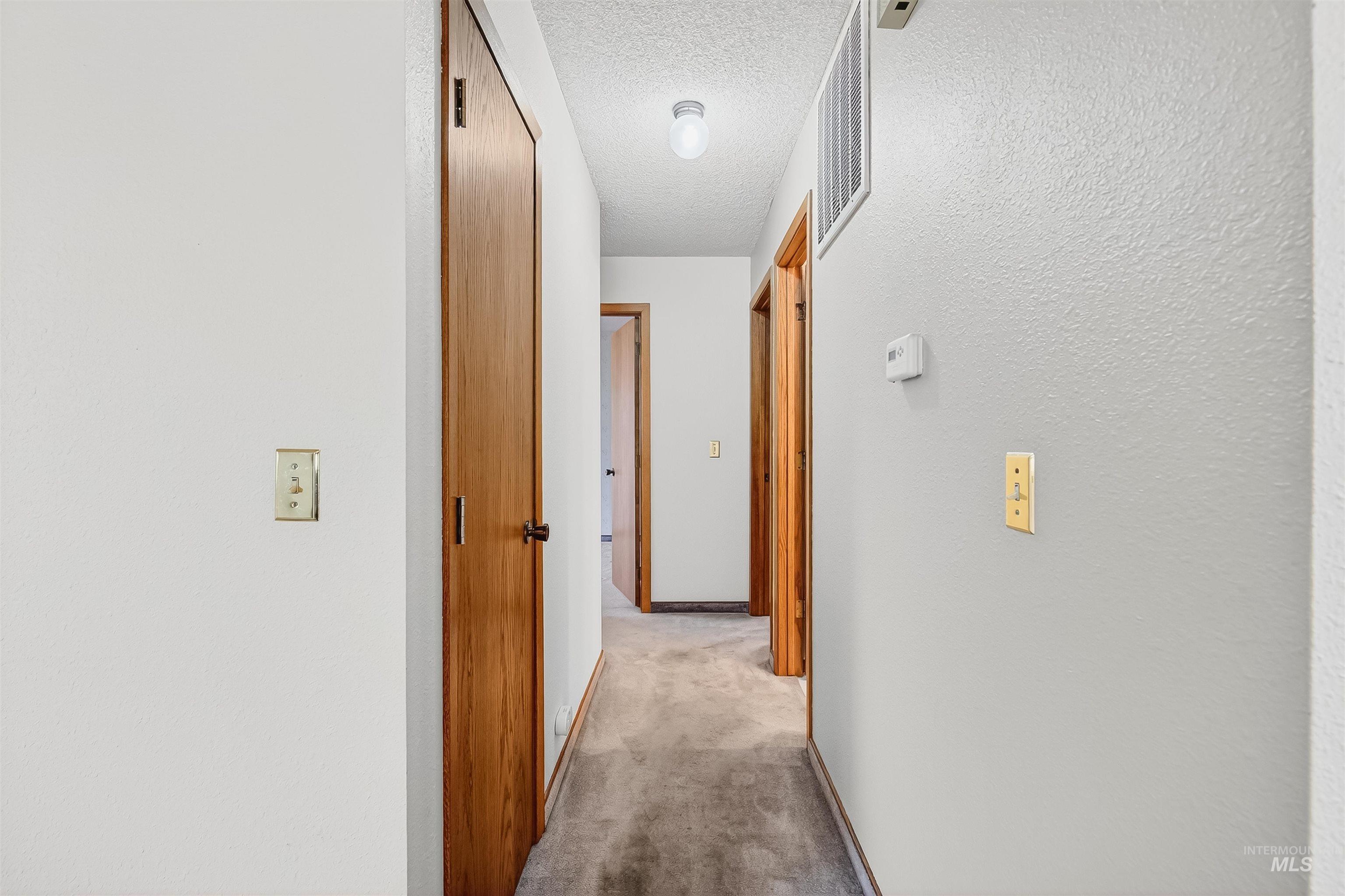 Hall with light colored carpet, a textured ceiling, and a textured wall