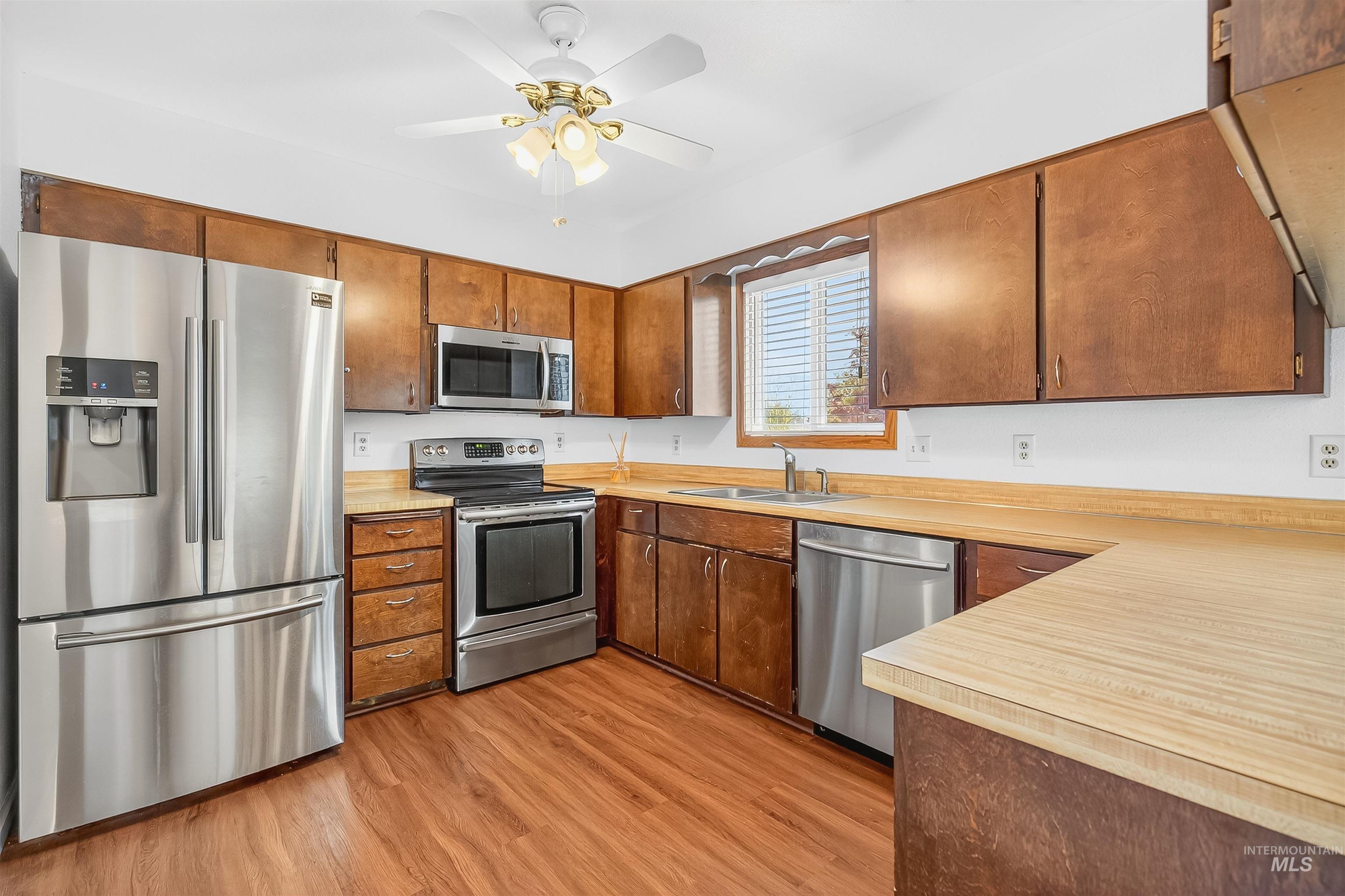 Kitchen featuring stainless steel appliances, light countertops, light wood finished floors, brown cabinetry, and a ceiling fan