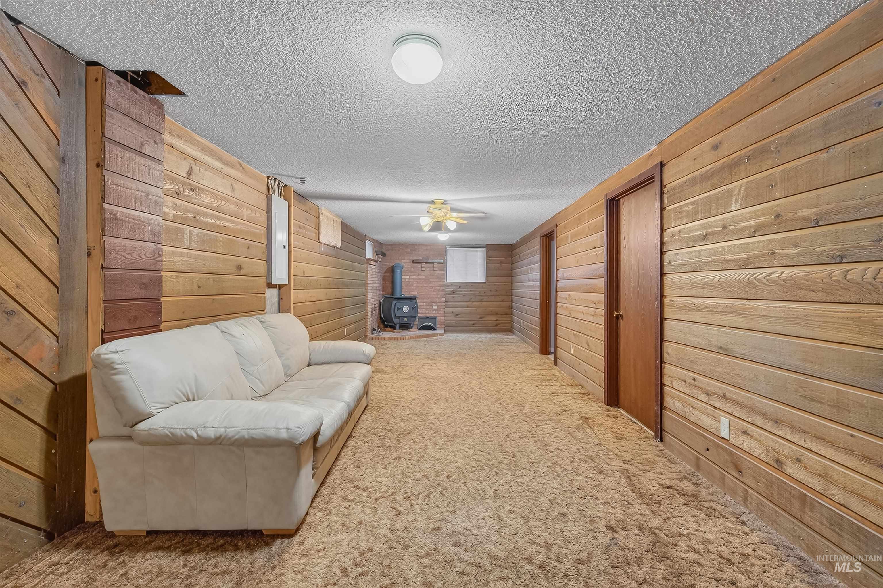 Sitting room featuring a wood stove, wooden walls, carpet, and a textured ceiling