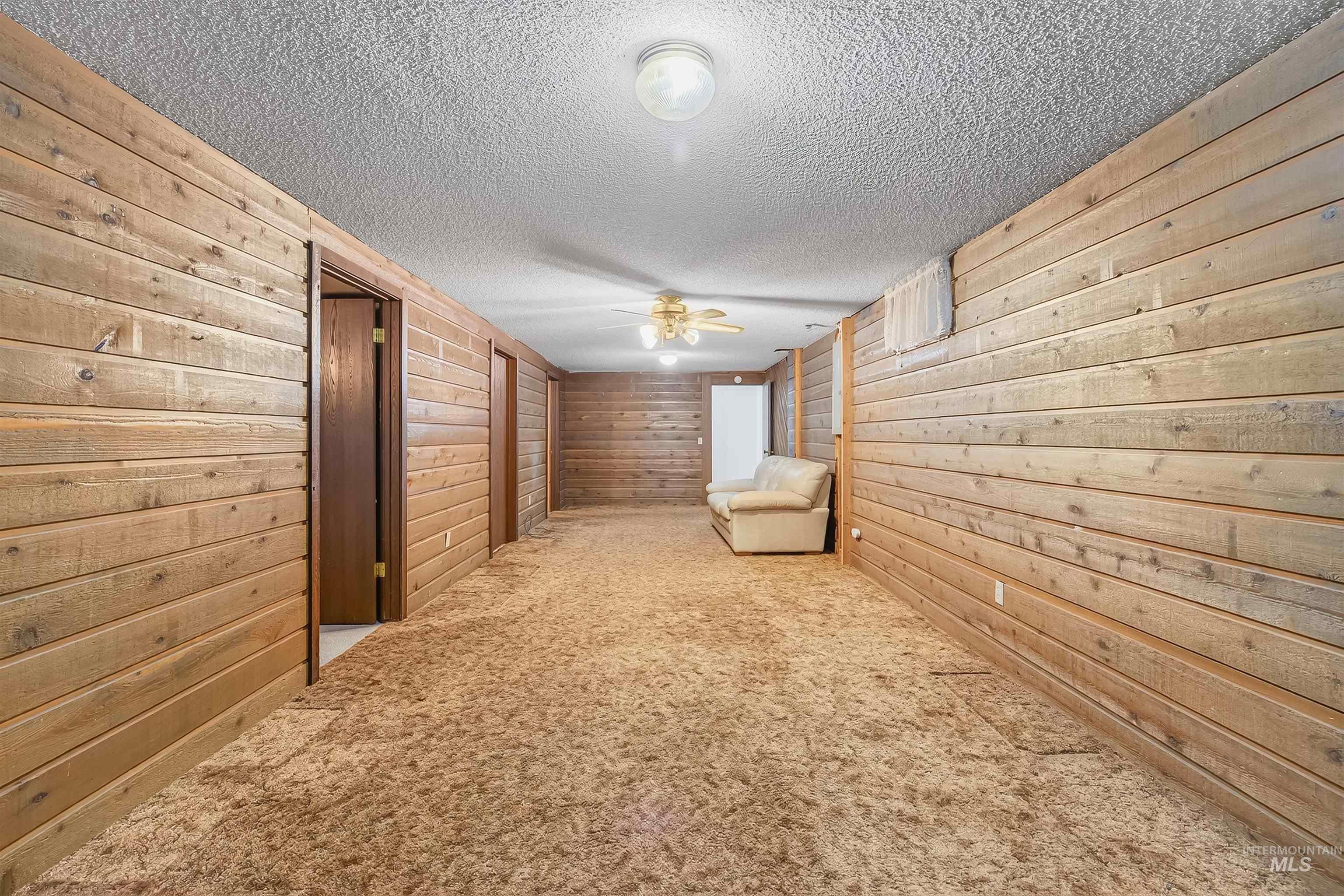 Unfurnished room with carpet flooring, wooden walls, a textured ceiling, and a ceiling fan