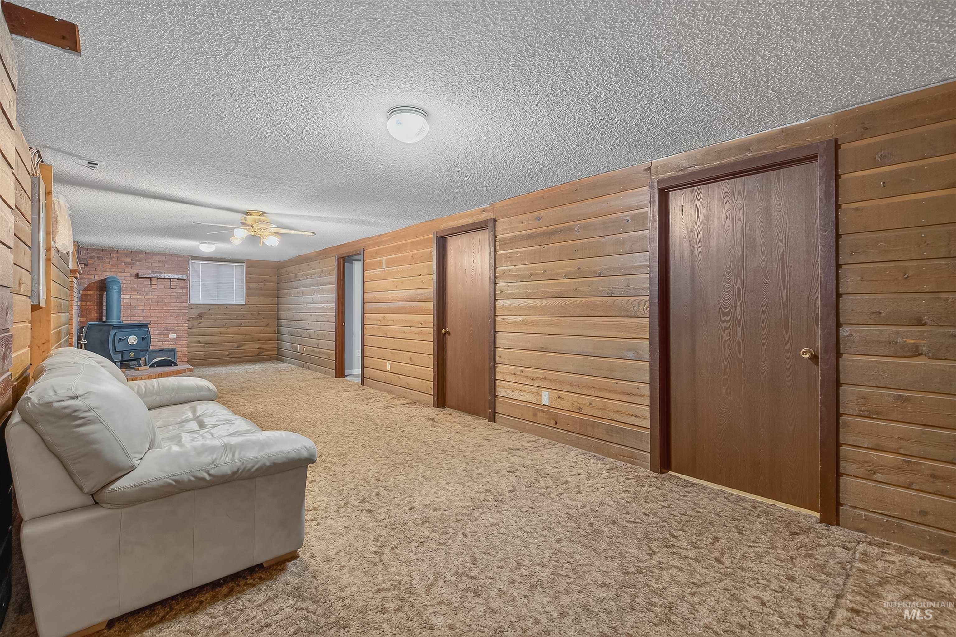 Carpeted living area featuring a wood stove, a textured ceiling, ceiling fan, and wood walls