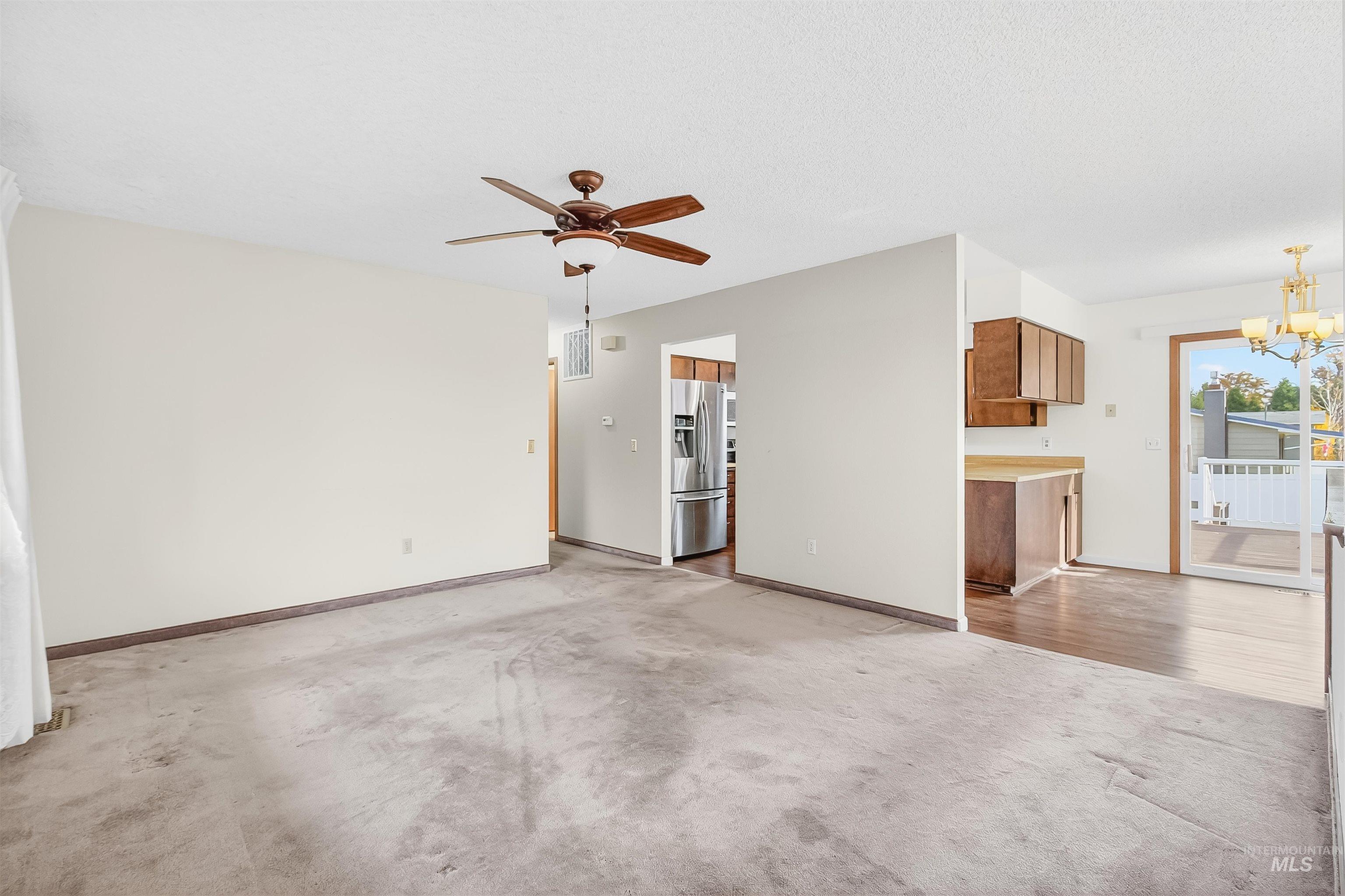 Unfurnished living room with light carpet, a chandelier, and ceiling fan