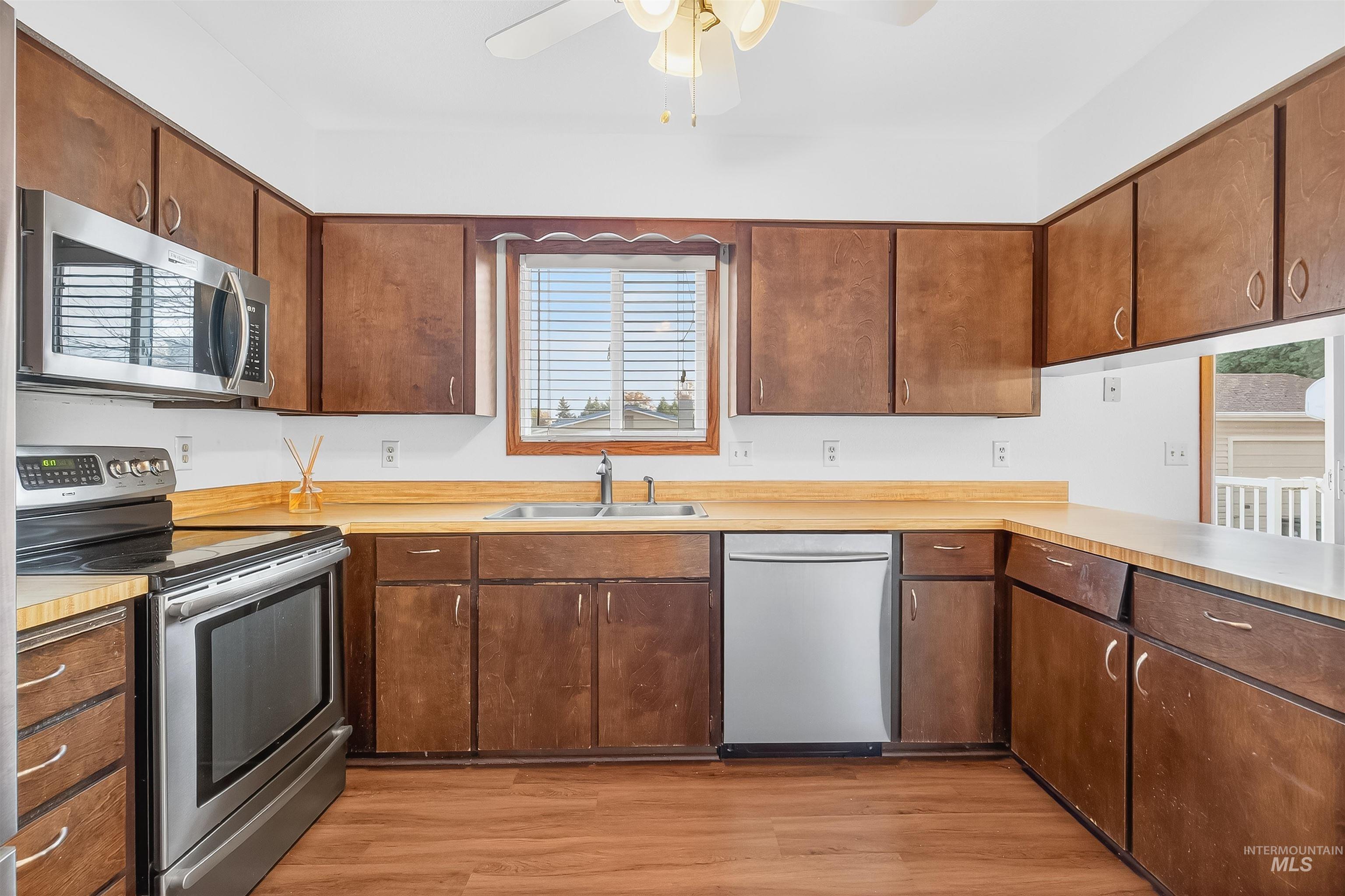 Kitchen with stainless steel appliances, light wood-style floors, light countertops, and a ceiling fan