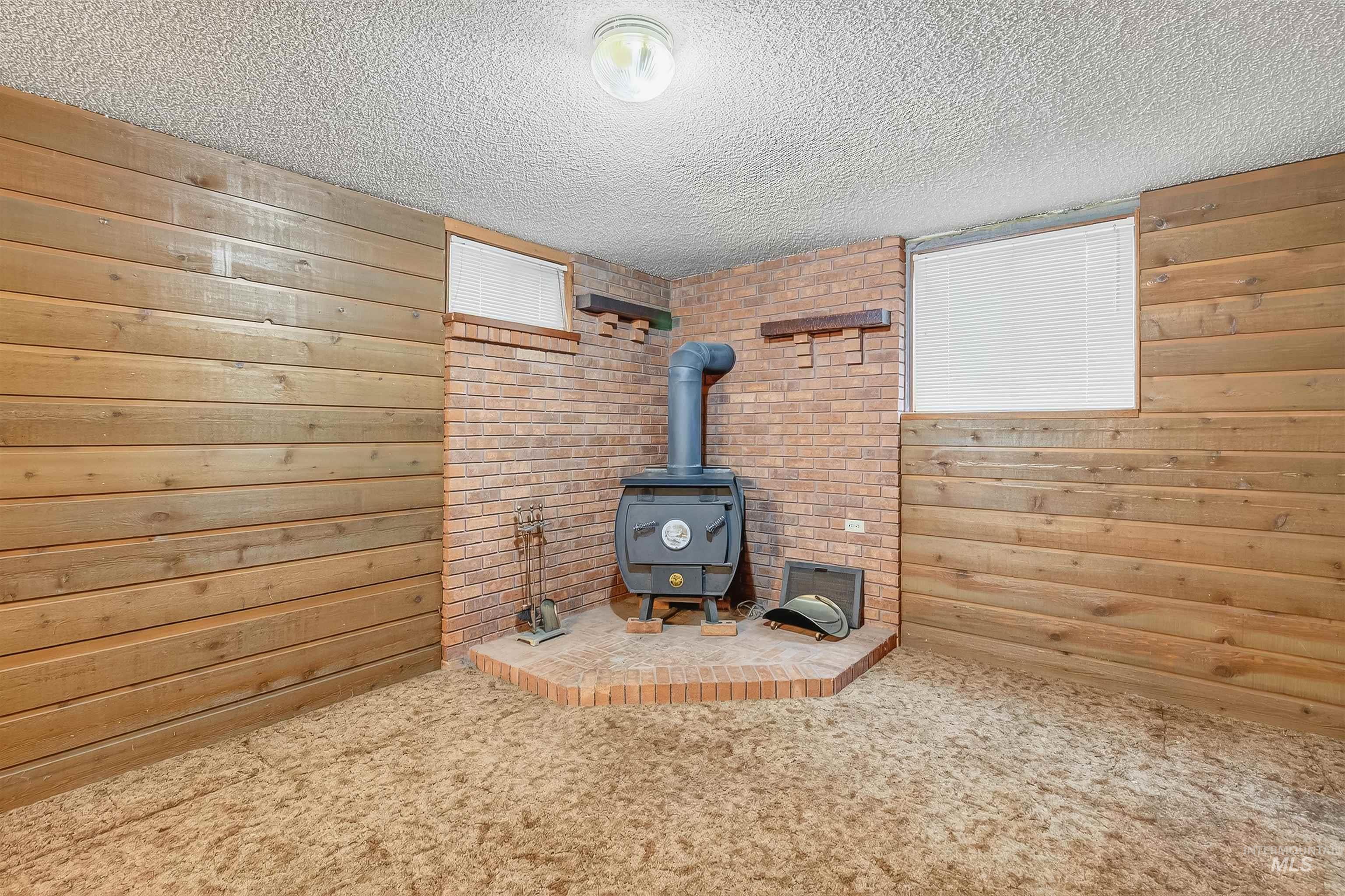 Detailed view of a wood stove, wooden walls, carpet floors, and a textured ceiling