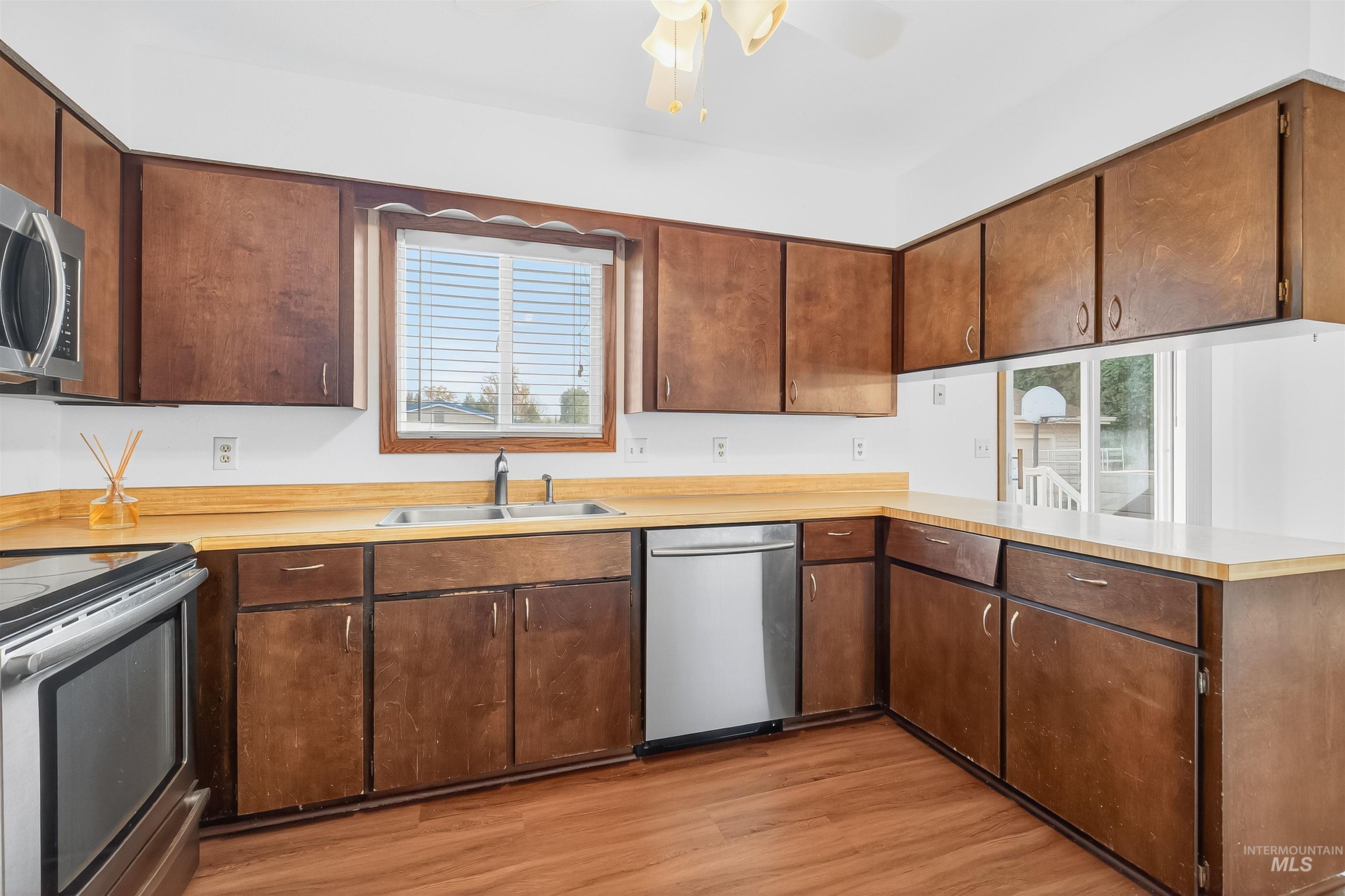 Kitchen with appliances with stainless steel finishes, light countertops, a peninsula, light wood finished floors, and ceiling fan