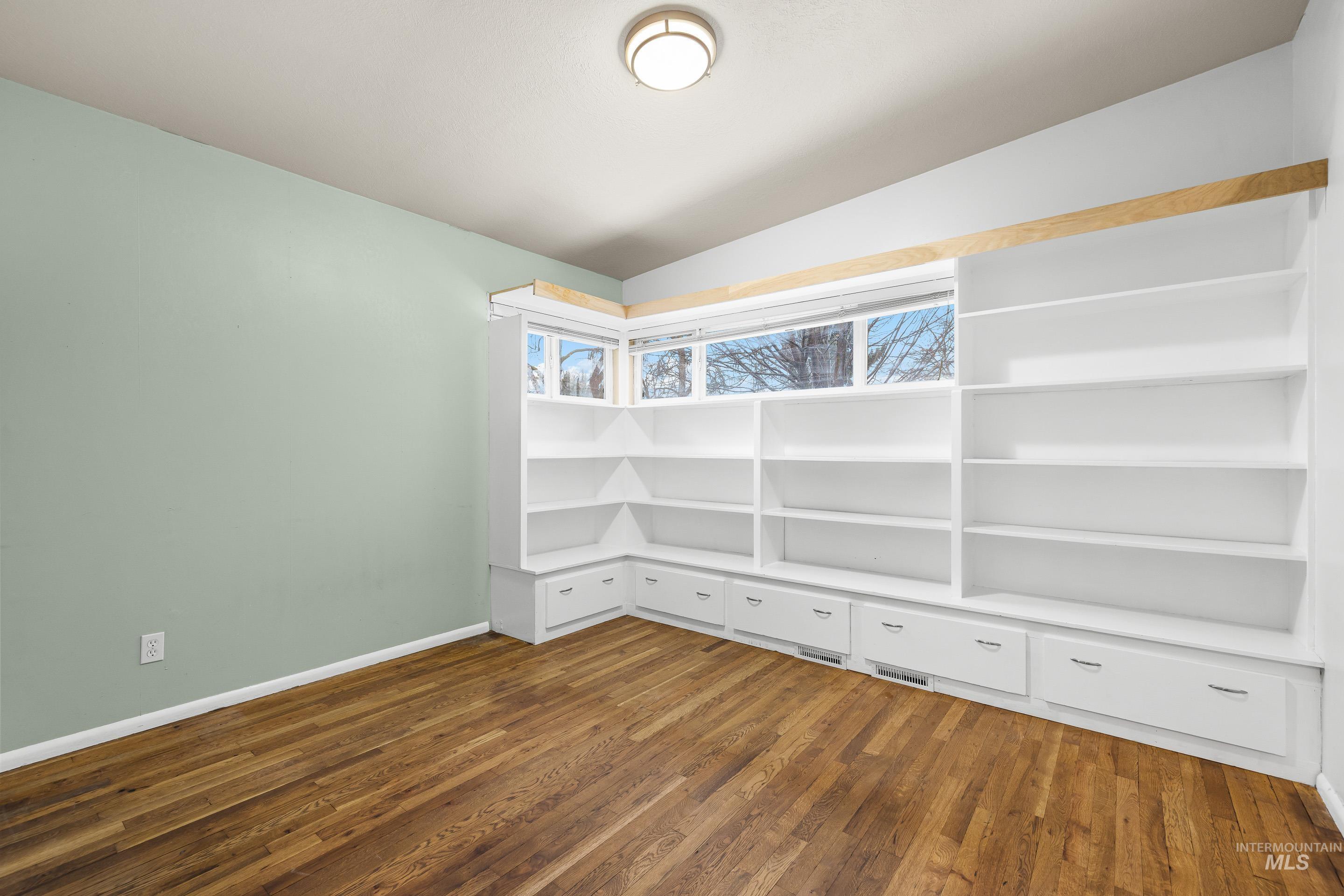 Empty room with vaulted ceiling and dark wood-style floors
