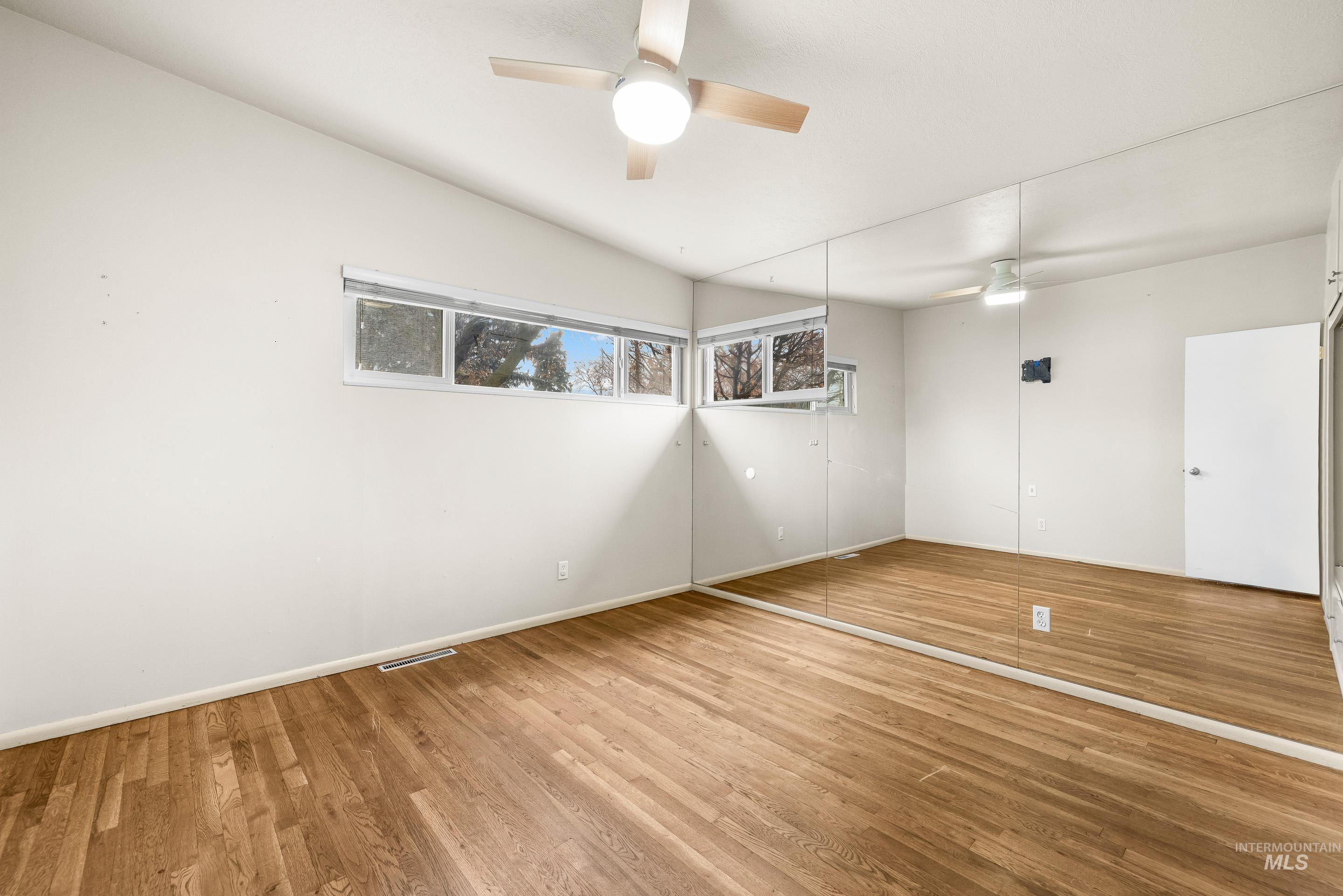 Unfurnished room with a ceiling fan, wood finished floors, and lofted ceiling