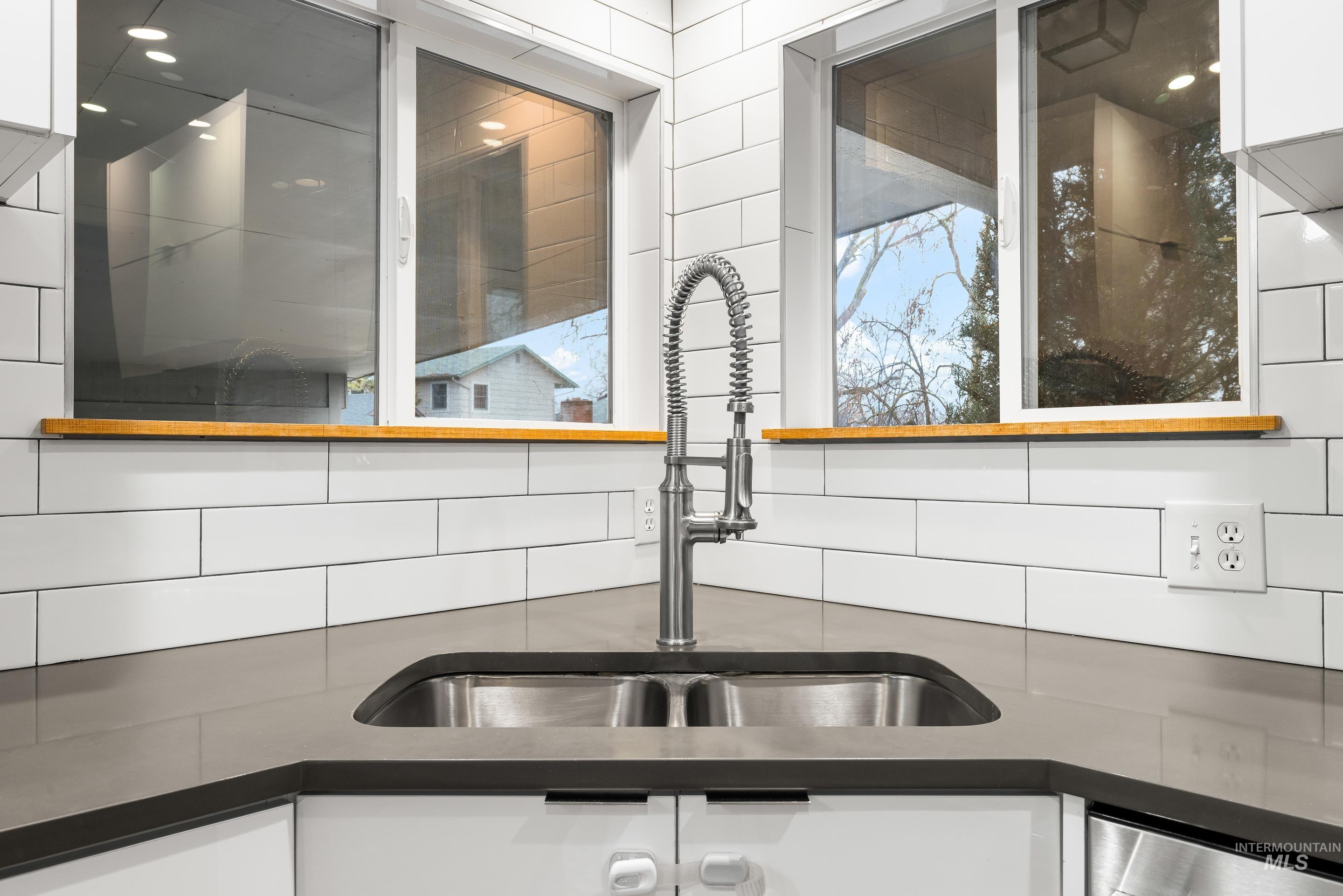 Kitchen view of white cabinetry, decorative backsplash, dark stone counters, and stainless steel dishwasher