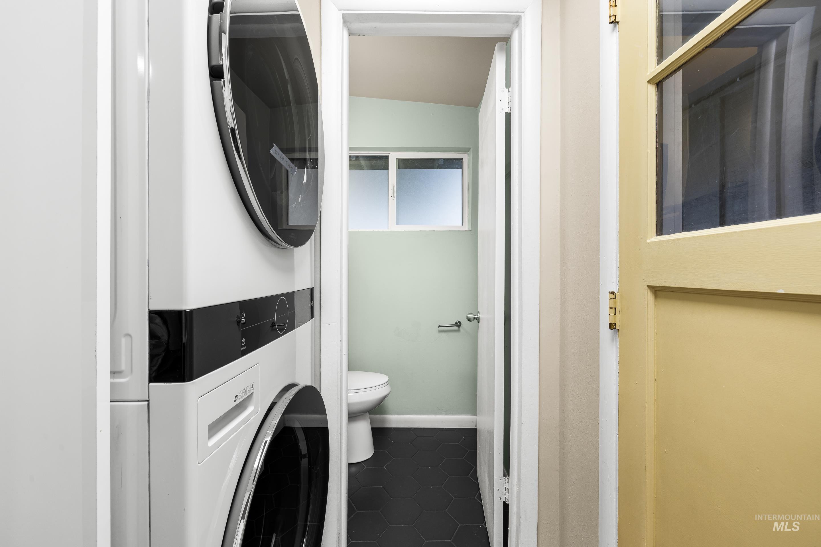 Laundry area featuring stacked washer / dryer and dark tile patterned flooring