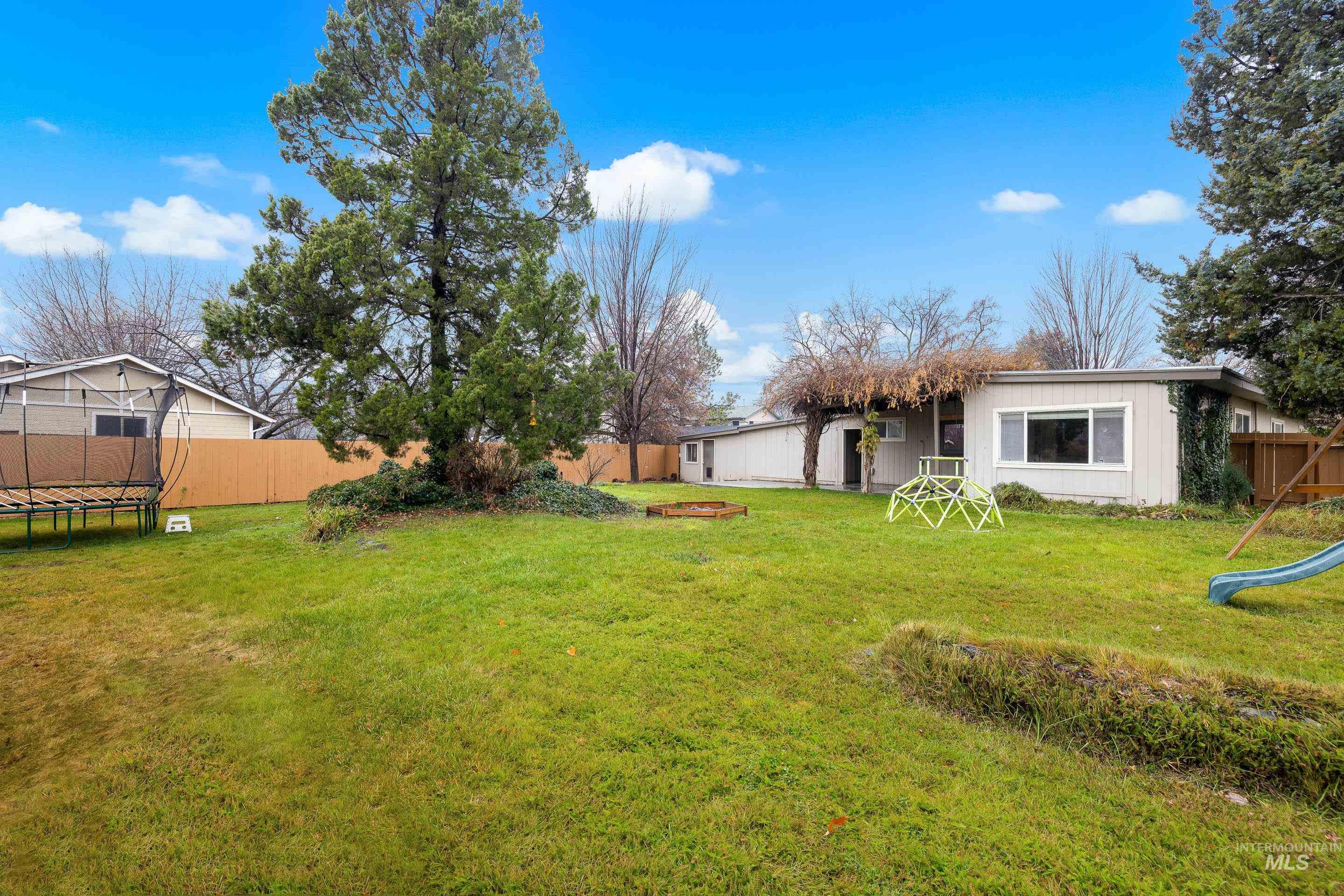 Fenced backyard featuring a trampoline and a playground