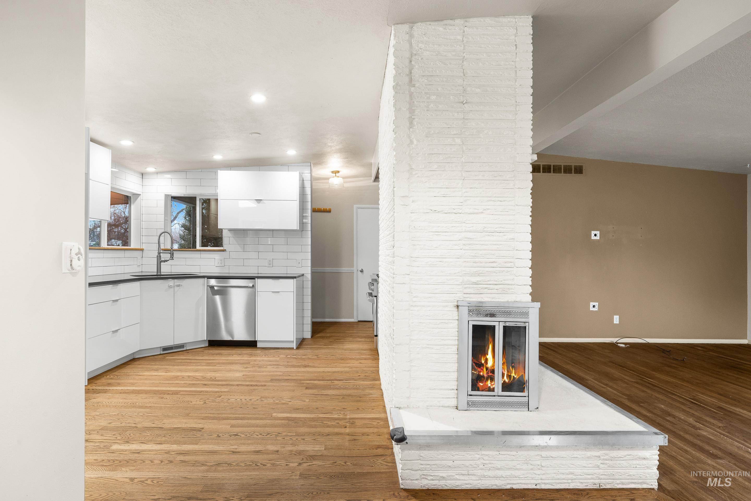 Kitchen with white cabinetry, dark countertops, tasteful backsplash, a fireplace, and stainless steel dishwasher