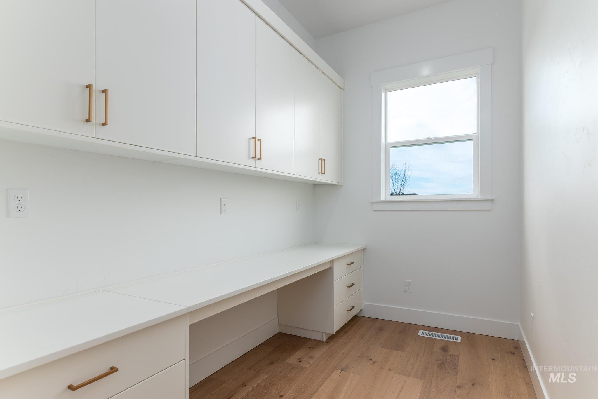 Integrated workstation with white cabinetry, ample countertop space, gold-tone hardware, and wood-finish flooring