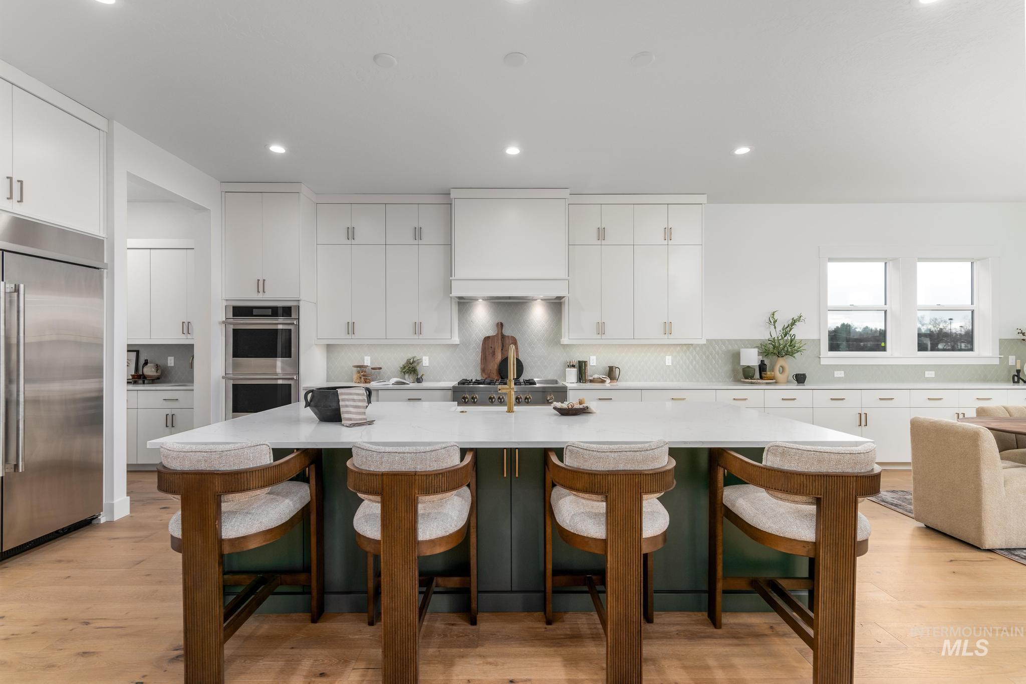 Spacious kitchen featuring a large island with seating, white shaker cabinetry, stainless steel appliances, and wood-finish flooring