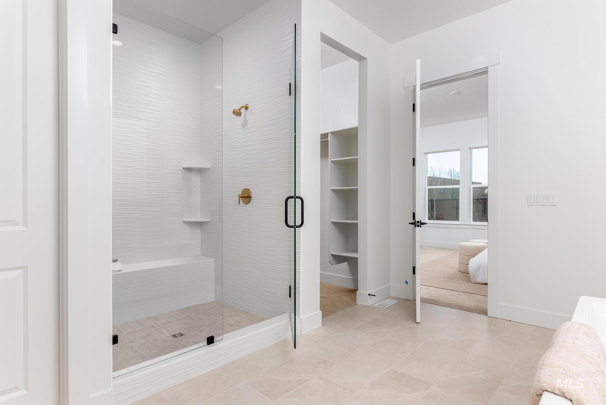 Spacious shower with clear glass enclosure, textured tile surround, built-in bench, and gold-tone fixtures
